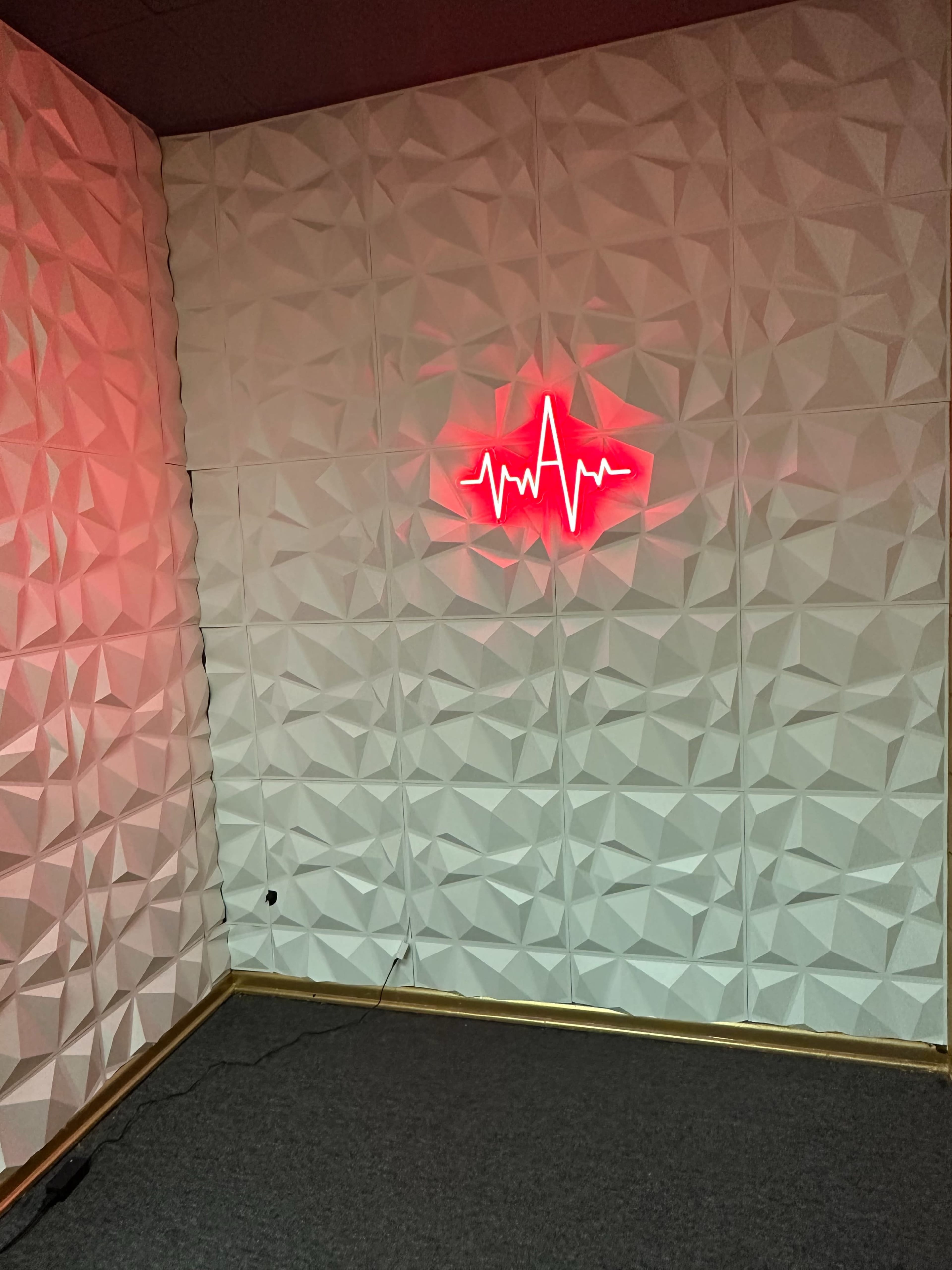 A corner of a room featuring a textured white wall and a red neon heartbeat sign.