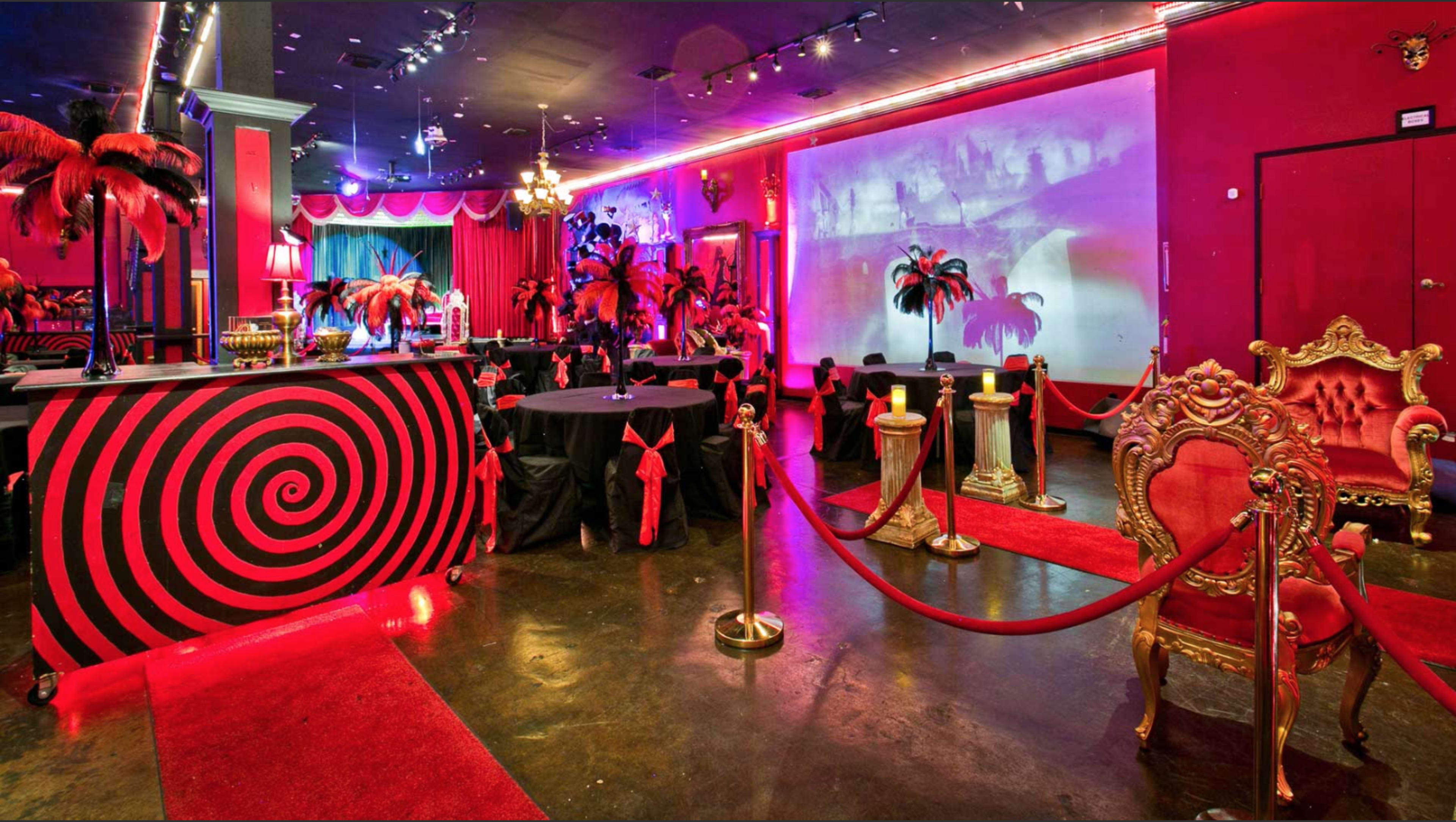 A vibrant party venue featuring a black and red color scheme, with a spiral-patterned bar, elegant seating, and decorative palm trees.