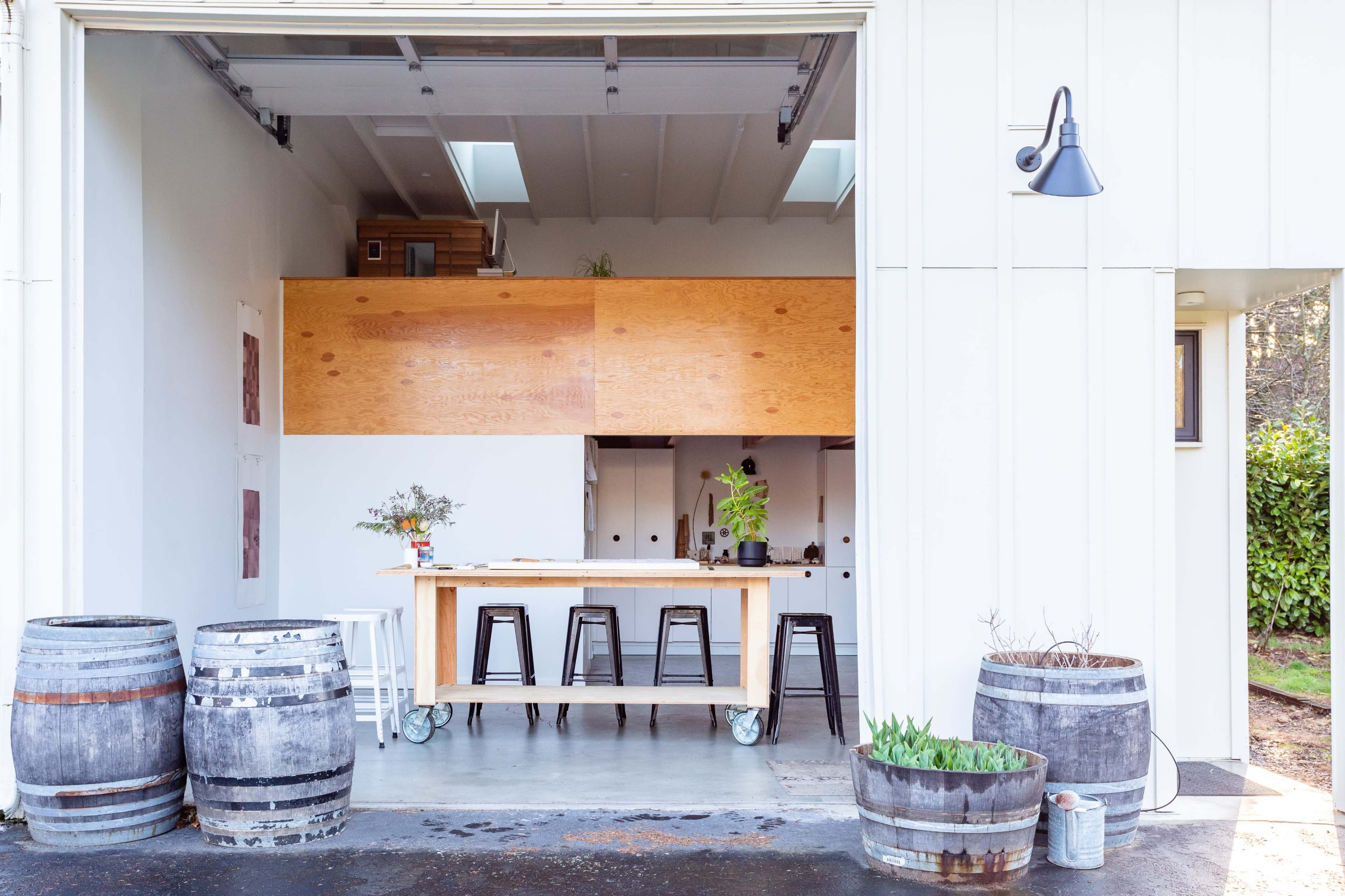 A modern, open space featuring a wooden counter with black stools and wooden barrels outside in front of a garage entryway.