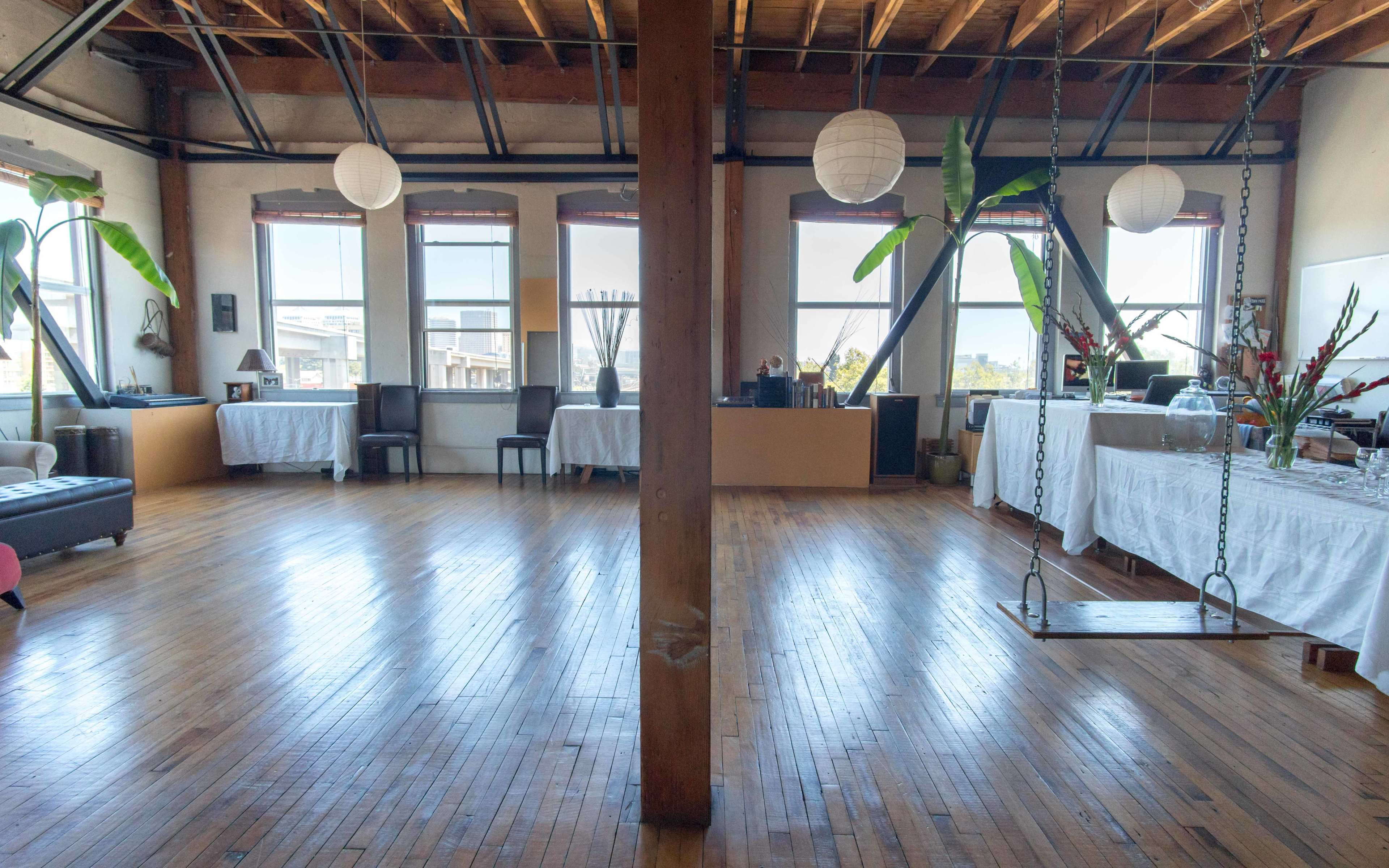 The room features hardwood floors, large windows with natural light, and a central wooden support column, with tables and chairs arranged on either side.