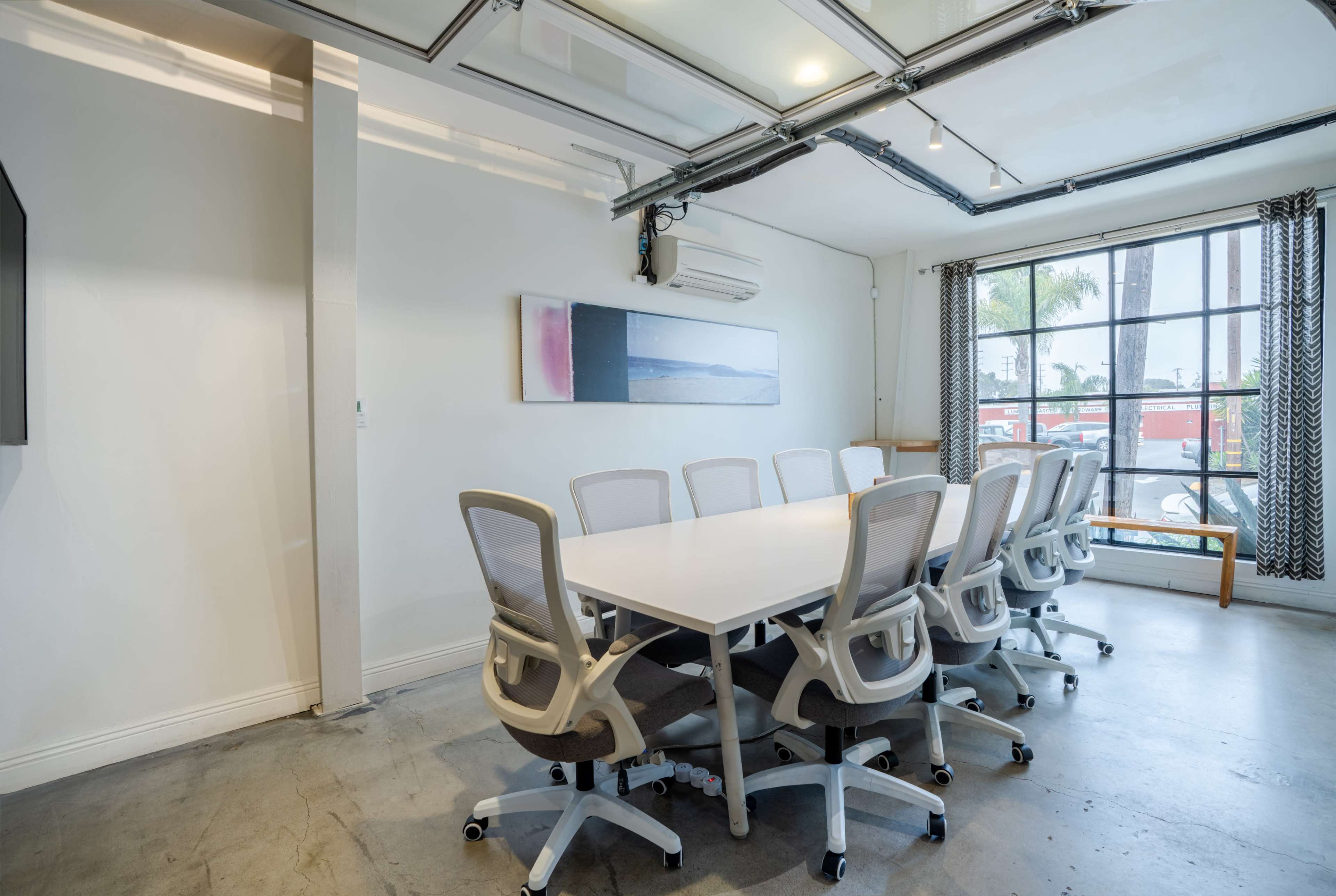 A modern conference room features a large white table surrounded by ergonomic chairs, with a window providing natural light and a view outside.