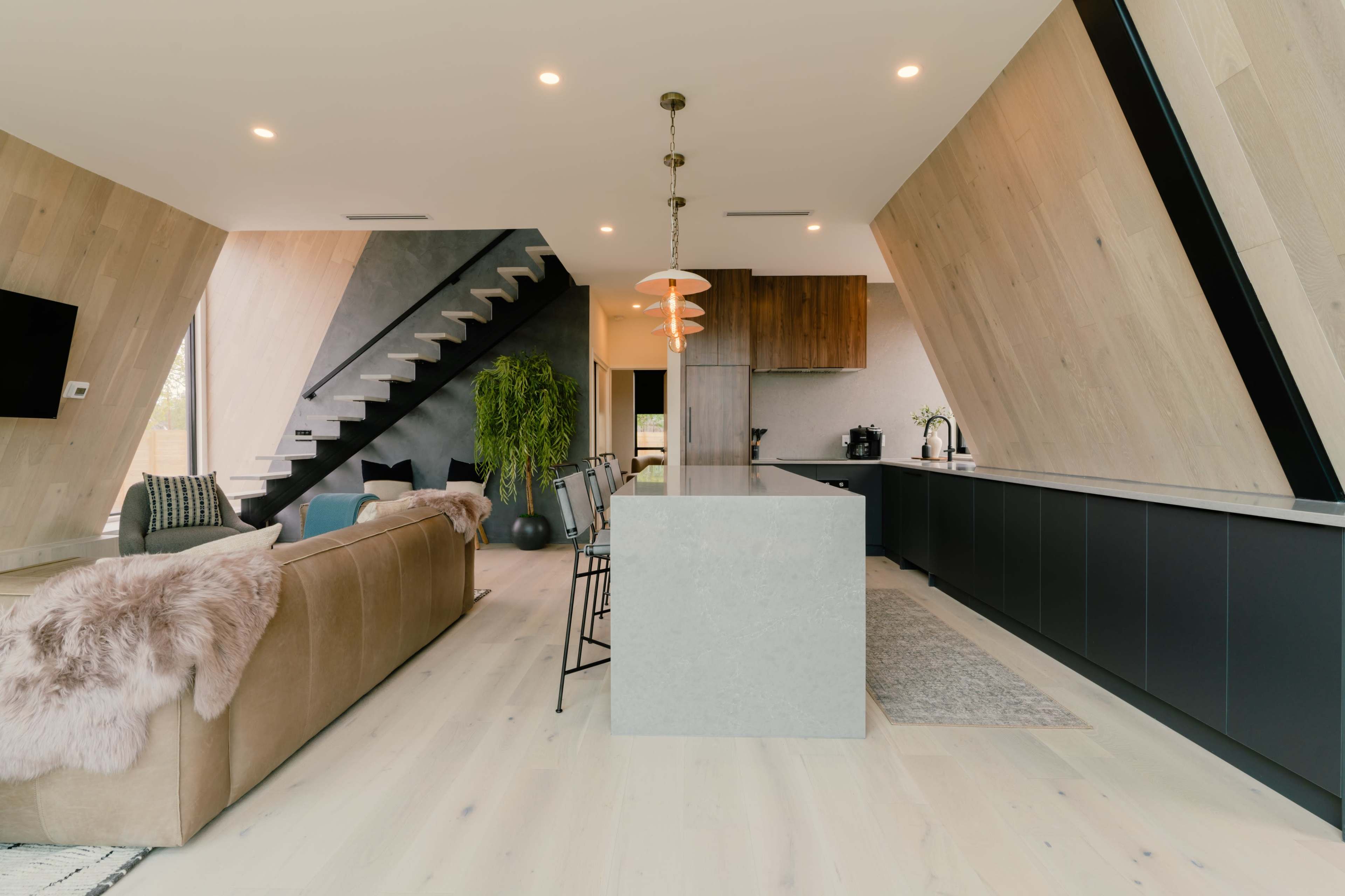 A modern kitchen and living area with slanted walls, a staircase, and a central island with bar seating.