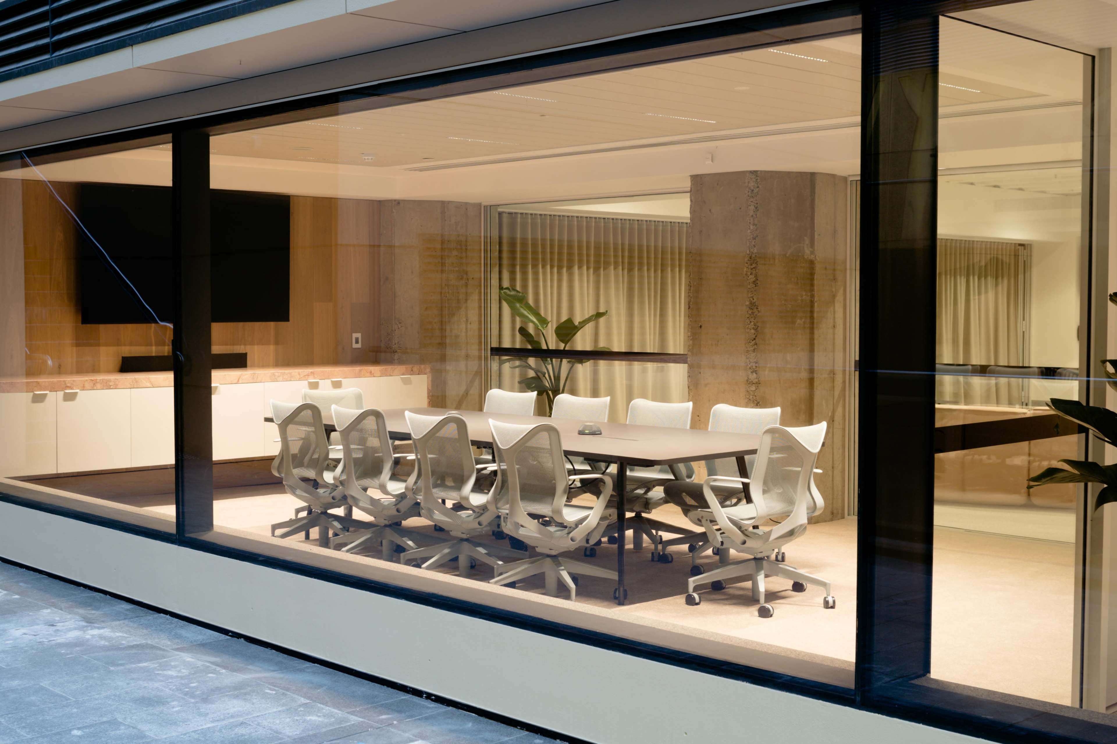 A modern conference room with a large table surrounded by white ergonomic chairs is visible through a glass wall.