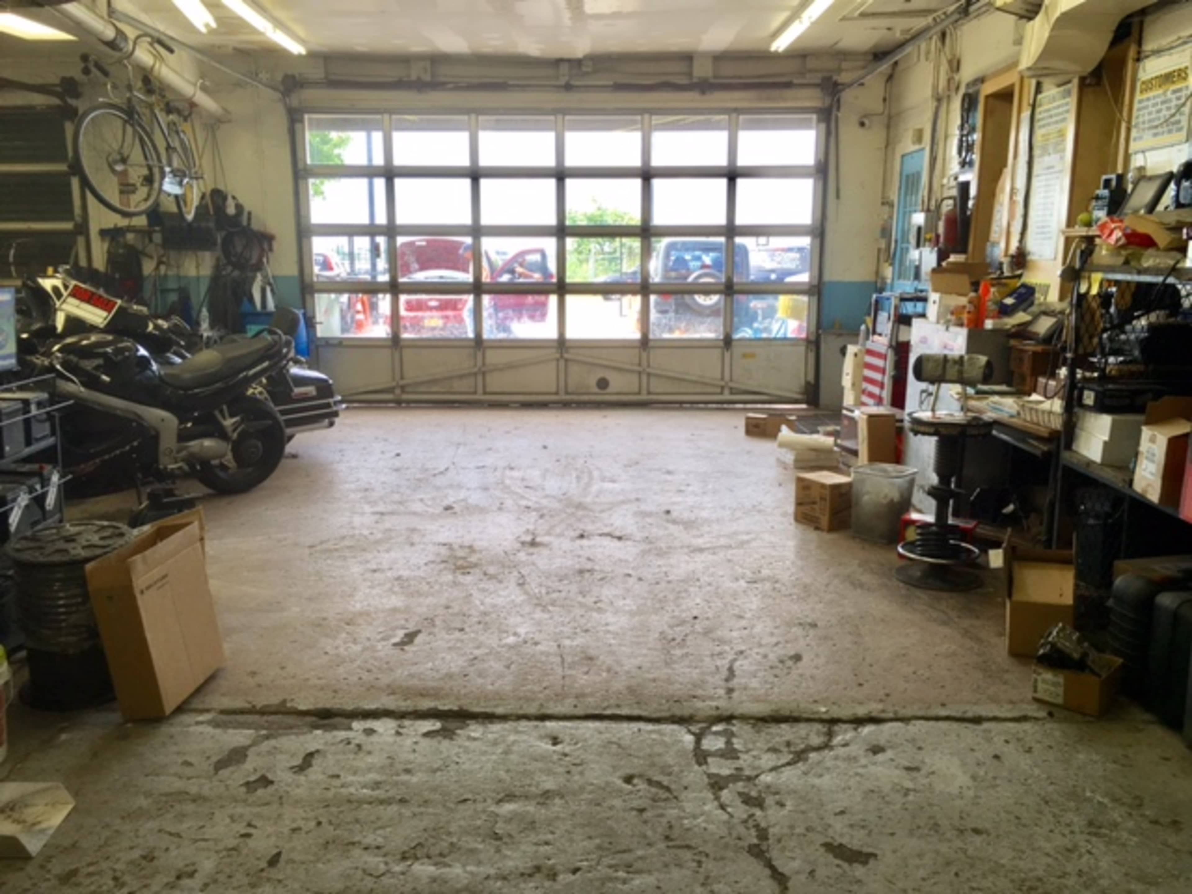 A spacious garage with a concrete floor, assorted boxes, and a motorcycle parked to one side, featuring large windows for natural light.