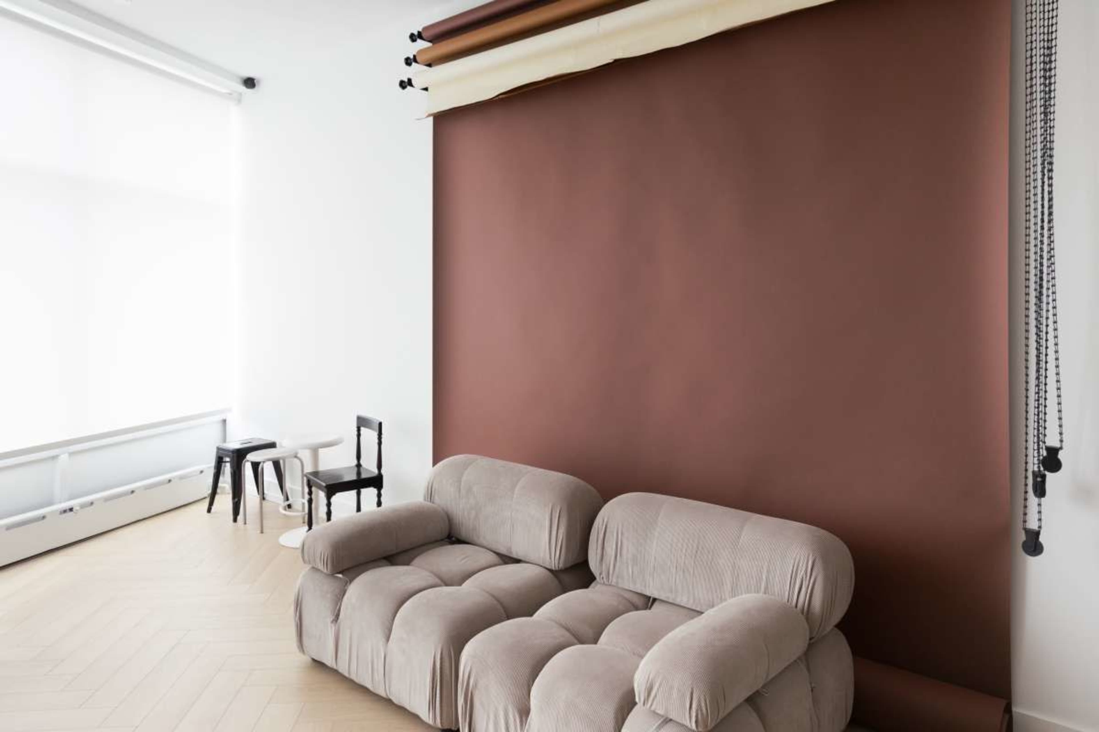 The image features a light-filled room with a brown backdrop, a beige couch, and minimalist furniture comprising two small tables.