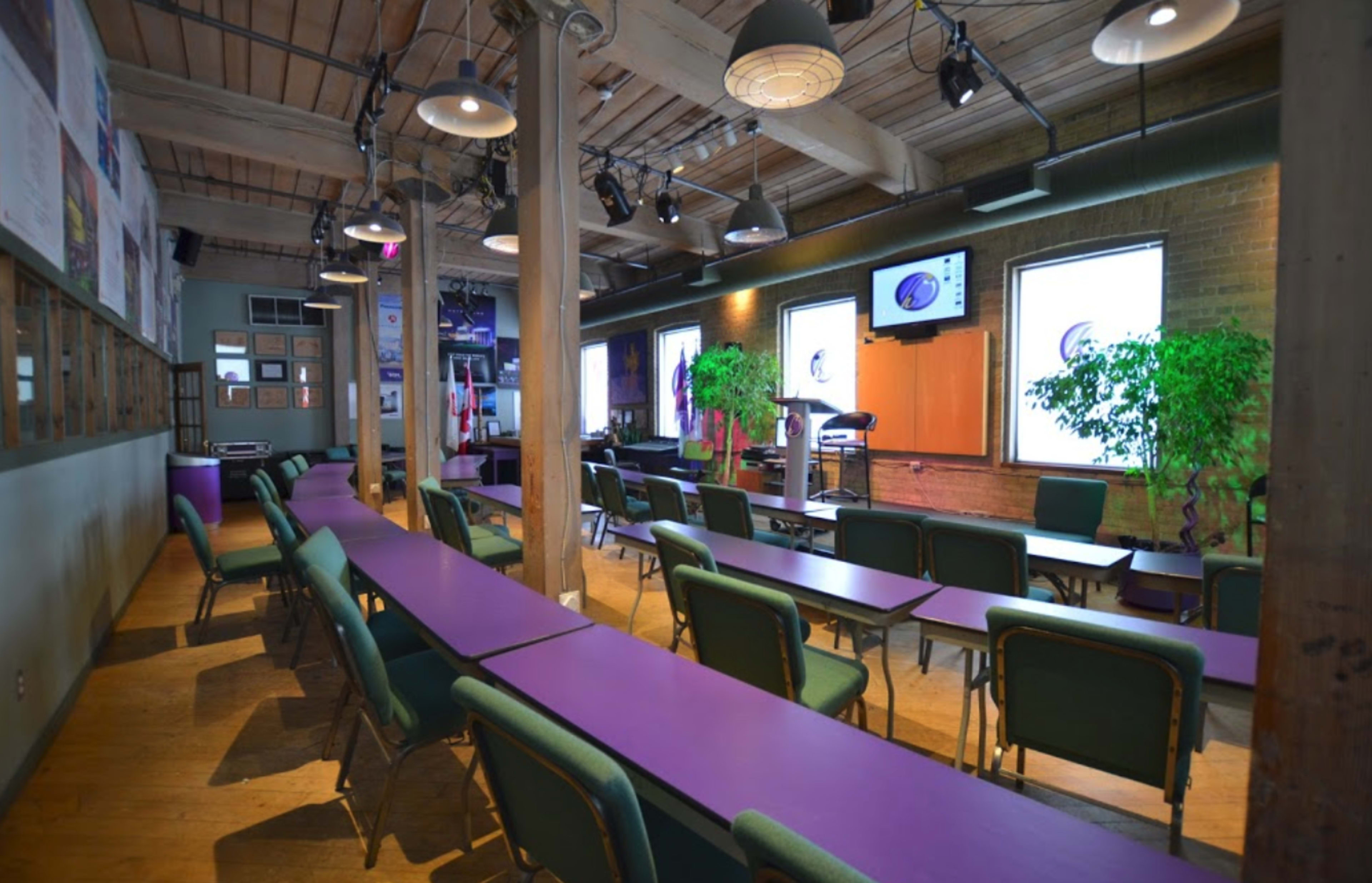 A classroom or meeting space with purple tables, green chairs, and large windows on one side.