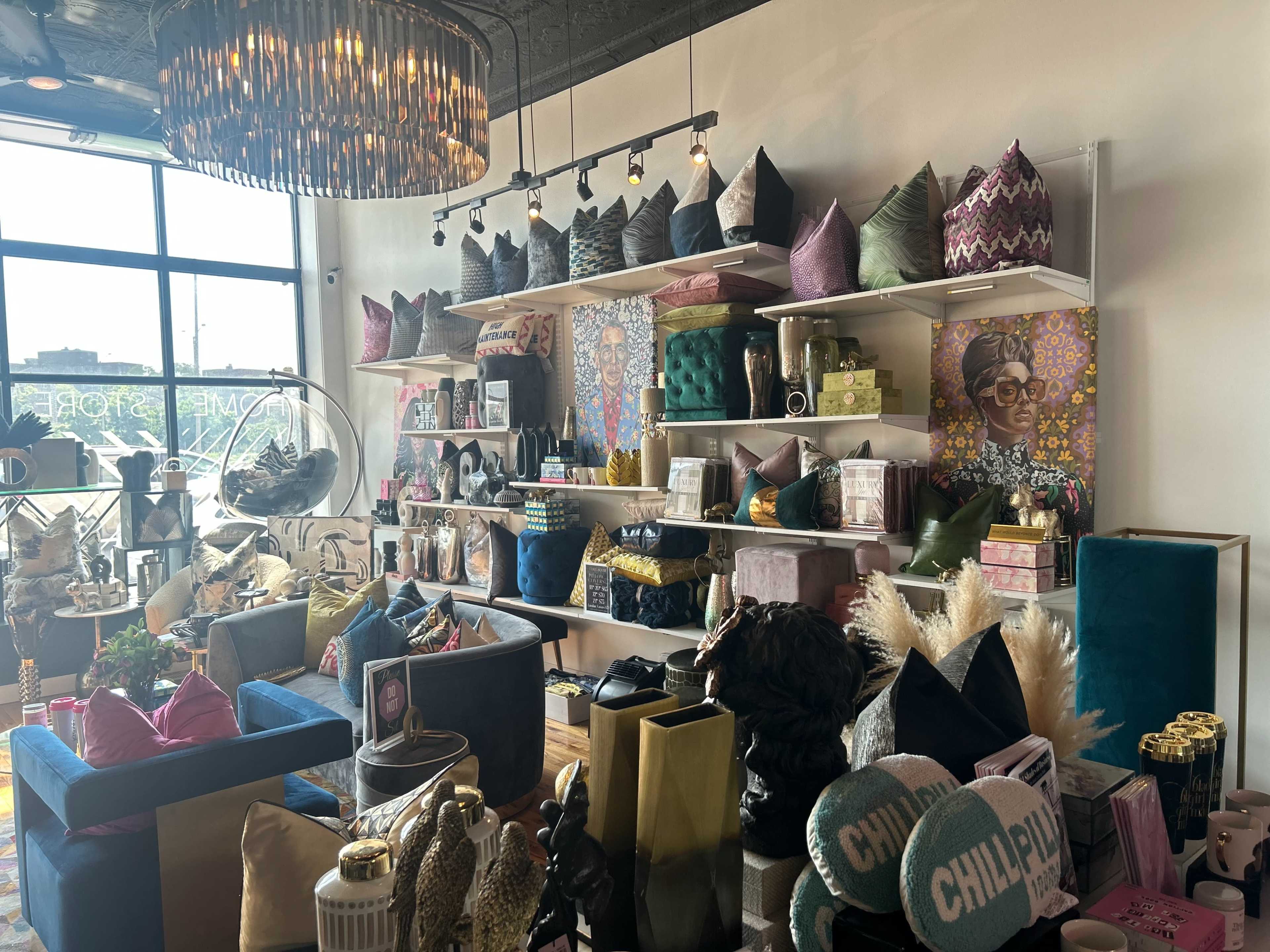 The interior of a retail store displays an arrangement of decorative pillows, unique decor items, and vibrant artwork on the shelves.