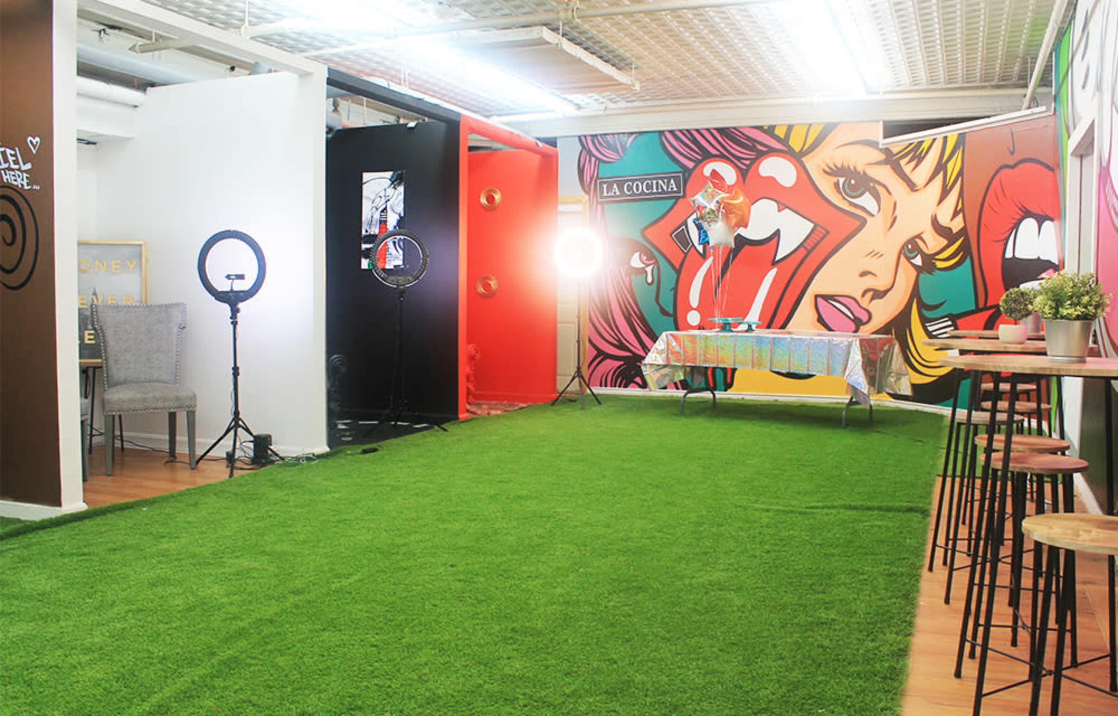 A room featuring artificial grass flooring, colorful wall murals, and tables set up for an event.