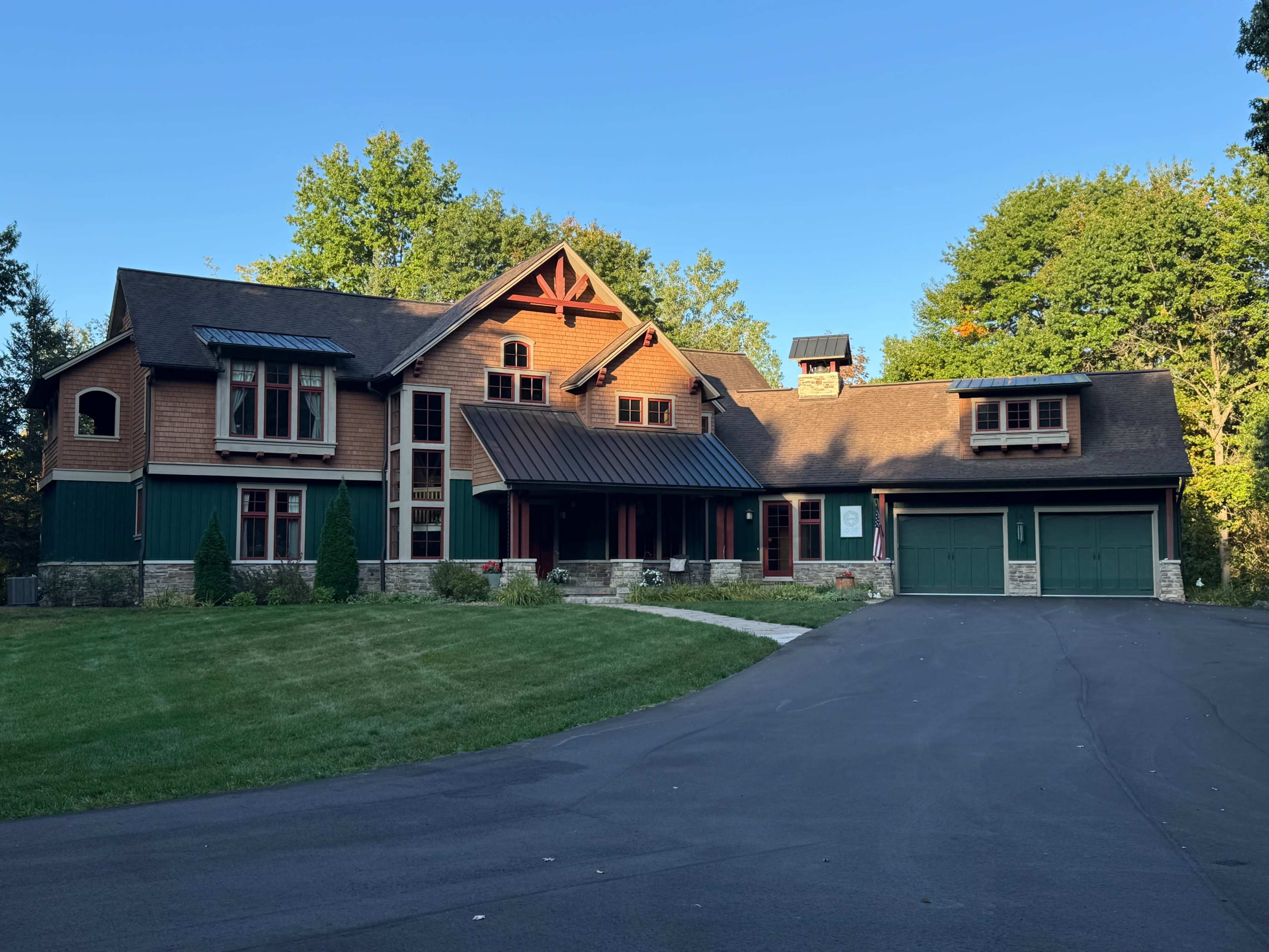 The image features a large, two-story house with a combination of wood and stone exterior, set on a lawn with trees in the background.