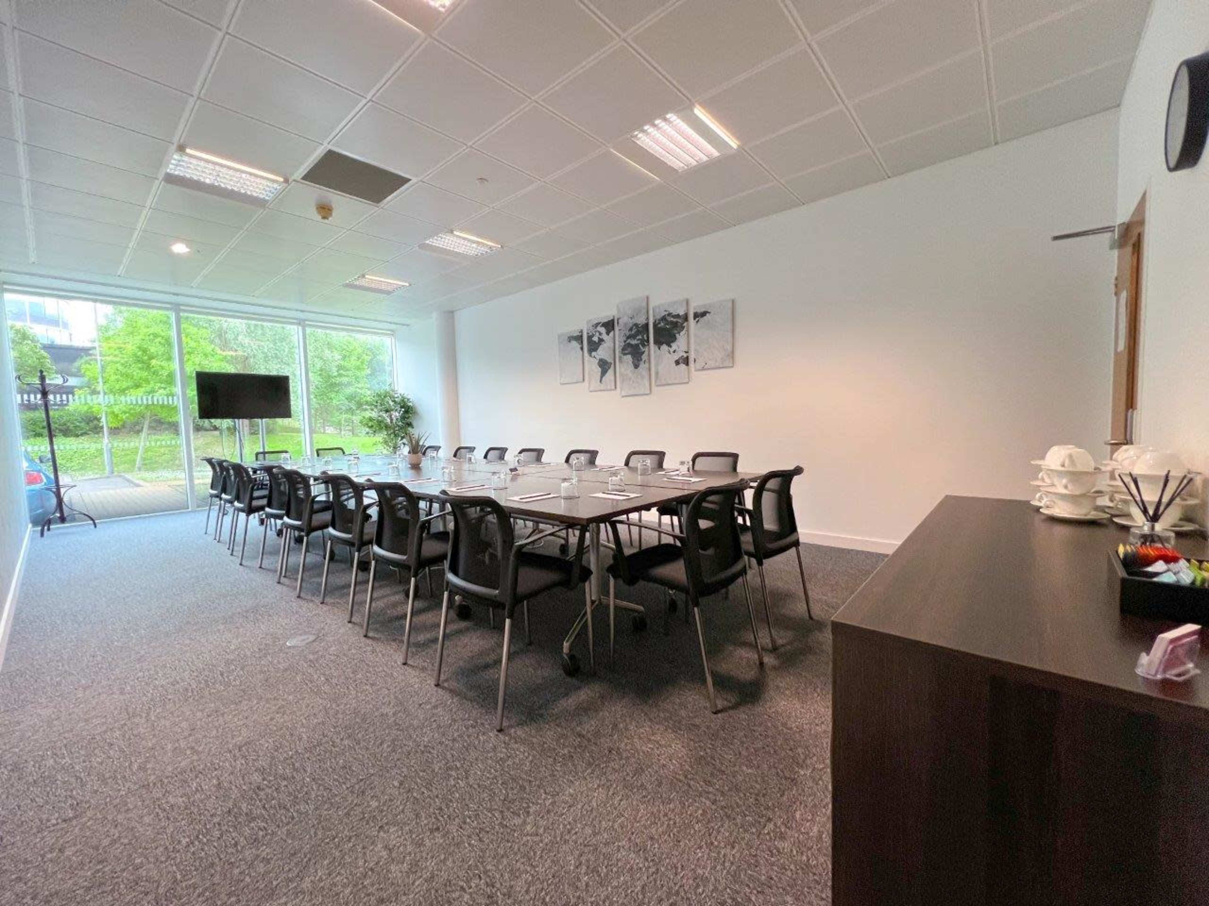 A conference room features a long table with chairs arranged around it, large windows providing natural light, and a side table with refreshments.