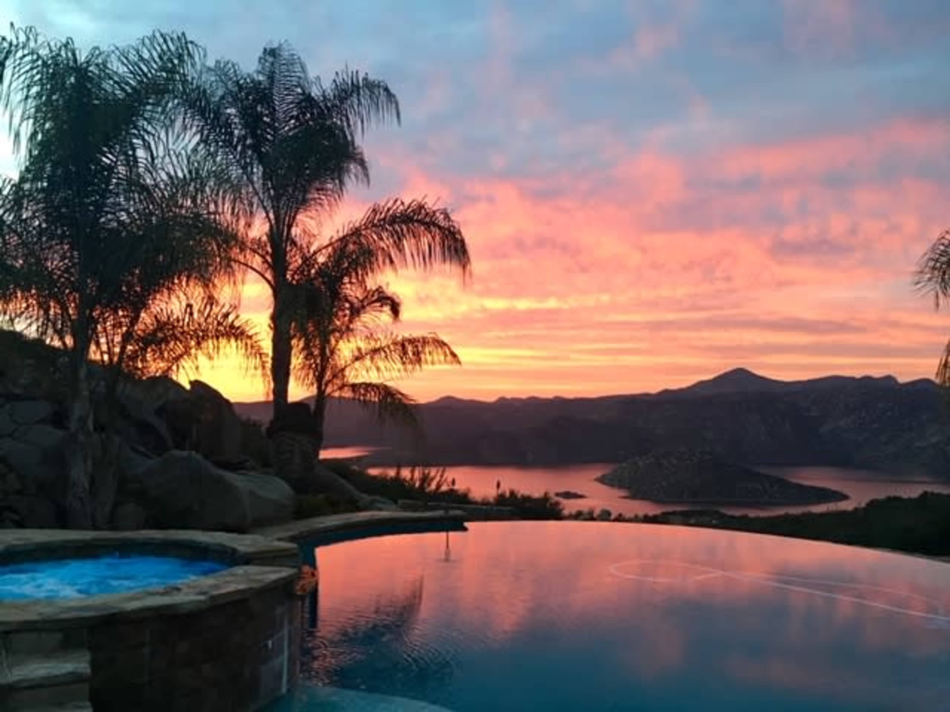 A tranquil infinity pool reflects the vibrant colors of a sunset over a mountainous landscape.