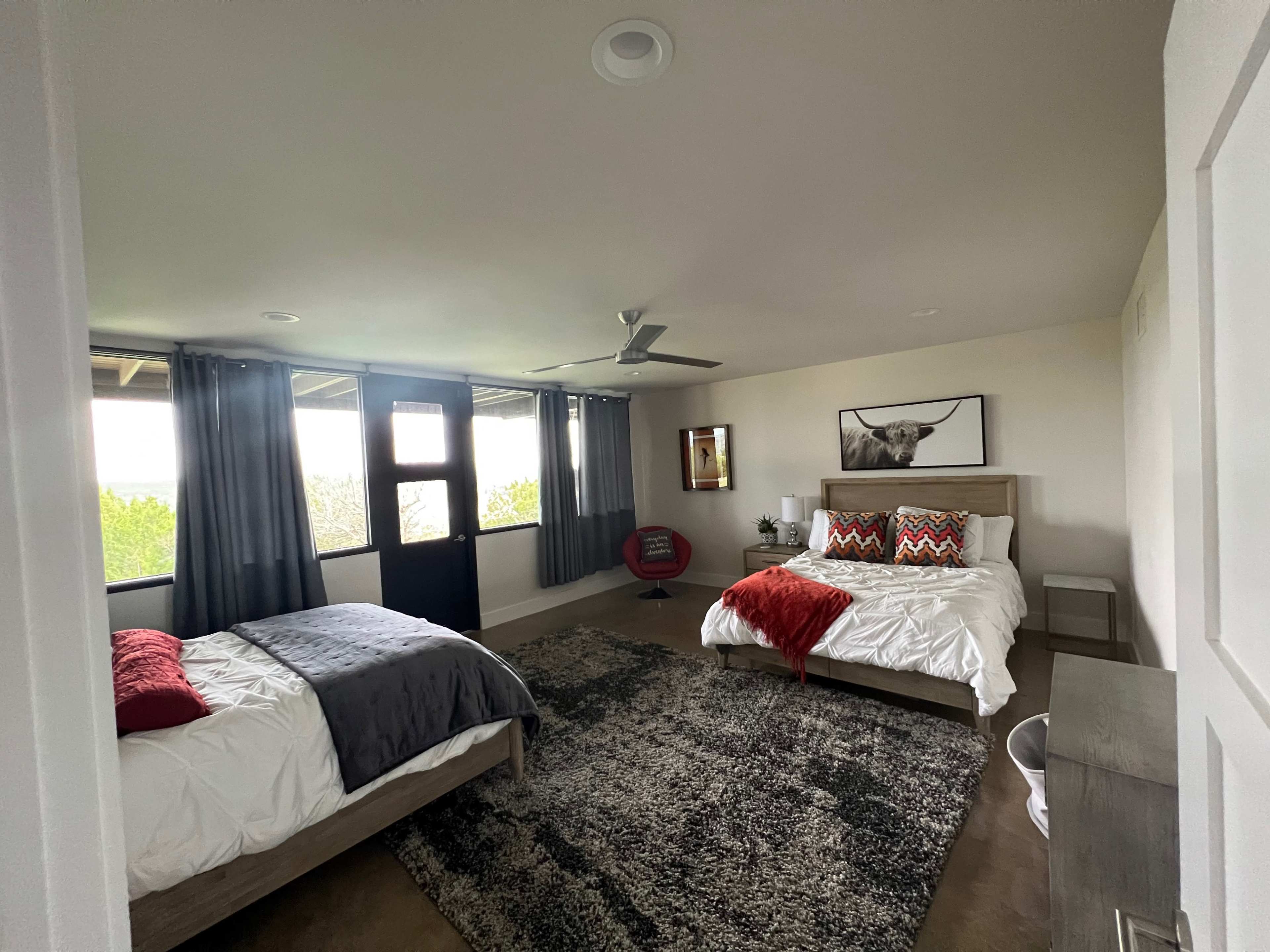 The image shows a spacious bedroom with two beds, large windows, and modern furnishings.