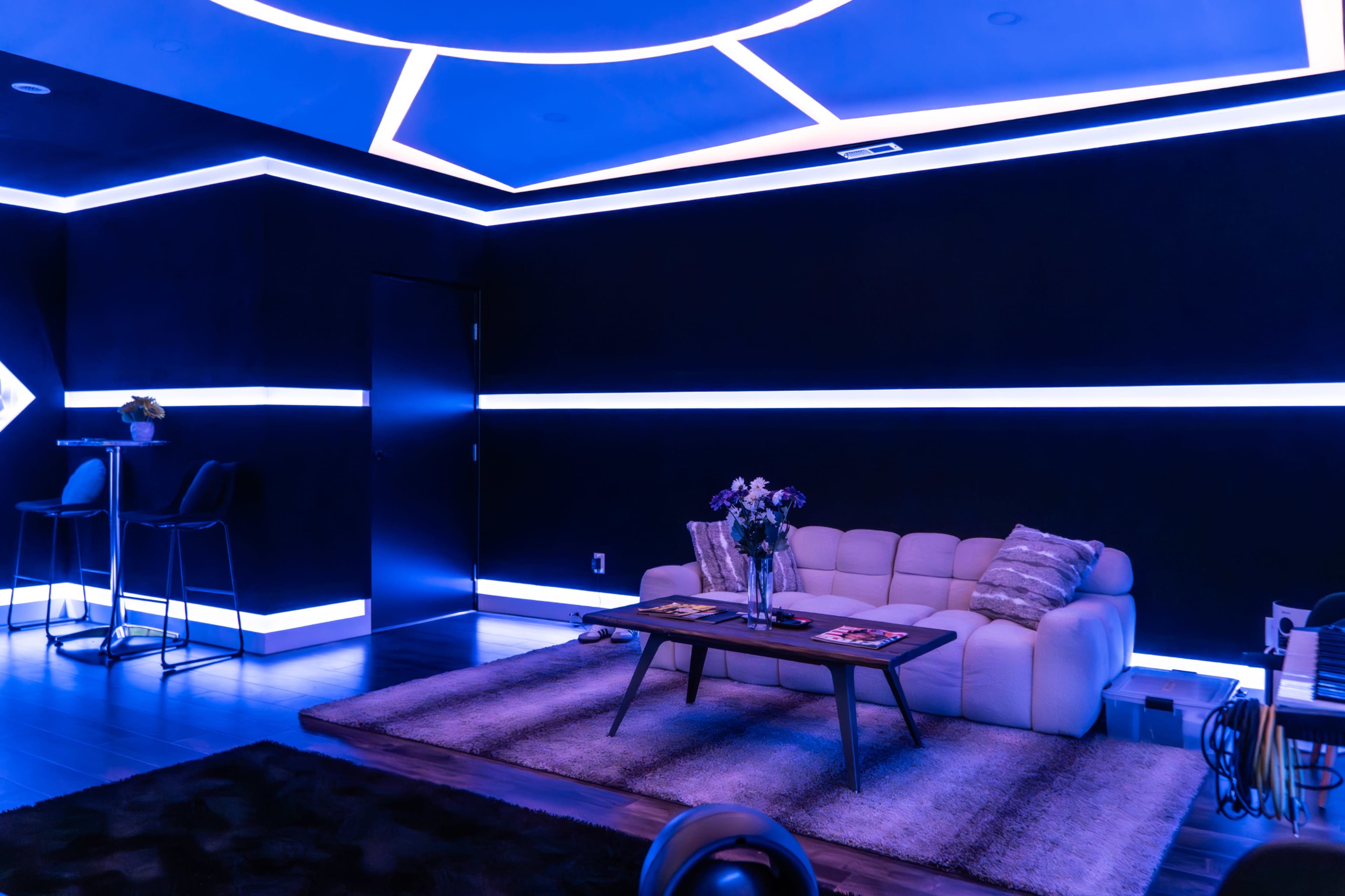 The image depicts a modern living room with a white sofa, a coffee table, and blue LED lighting along the walls and ceiling.