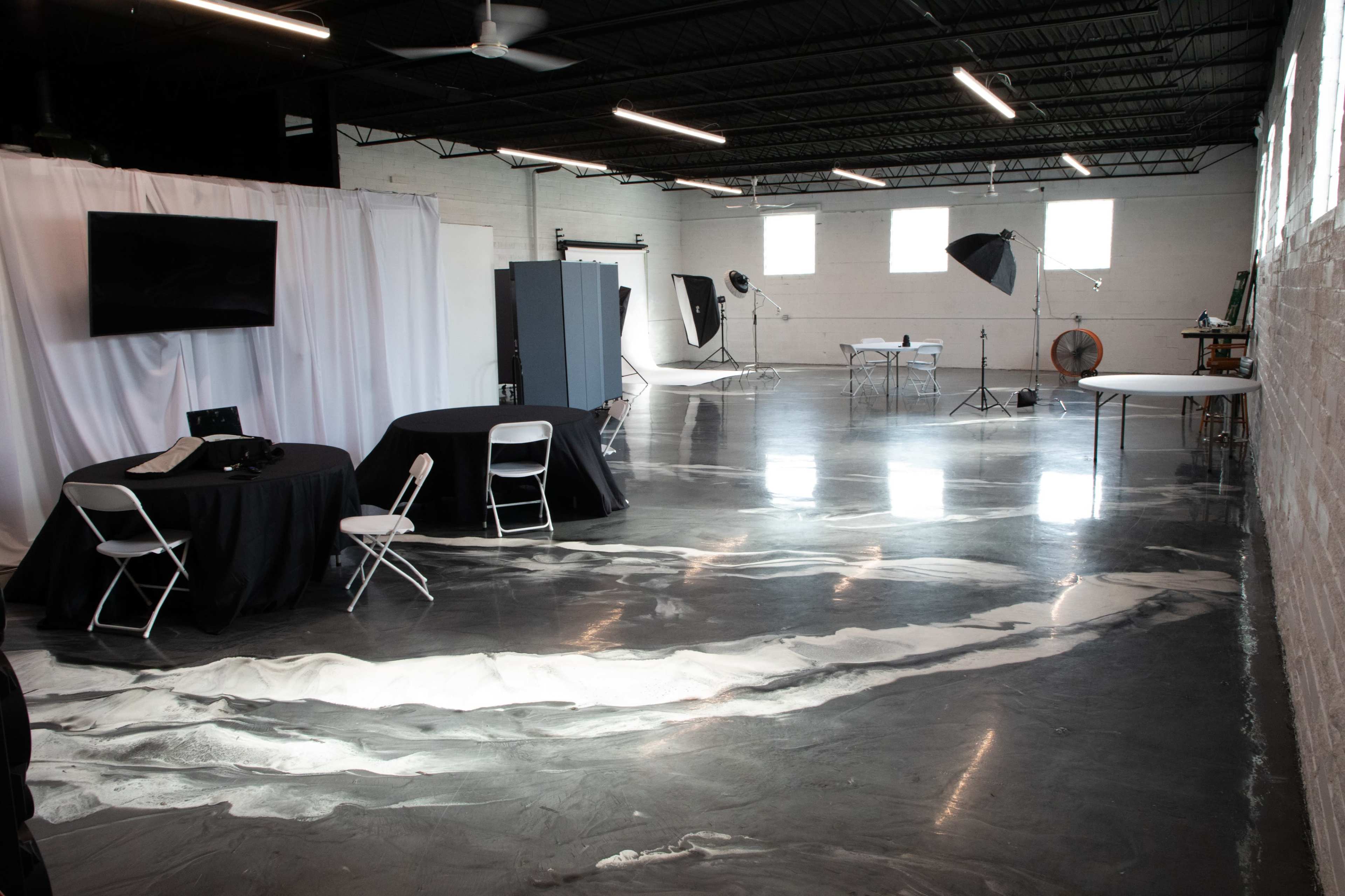 A spacious studio with polished gray floors, several tables and chairs, and various photography equipment set up.