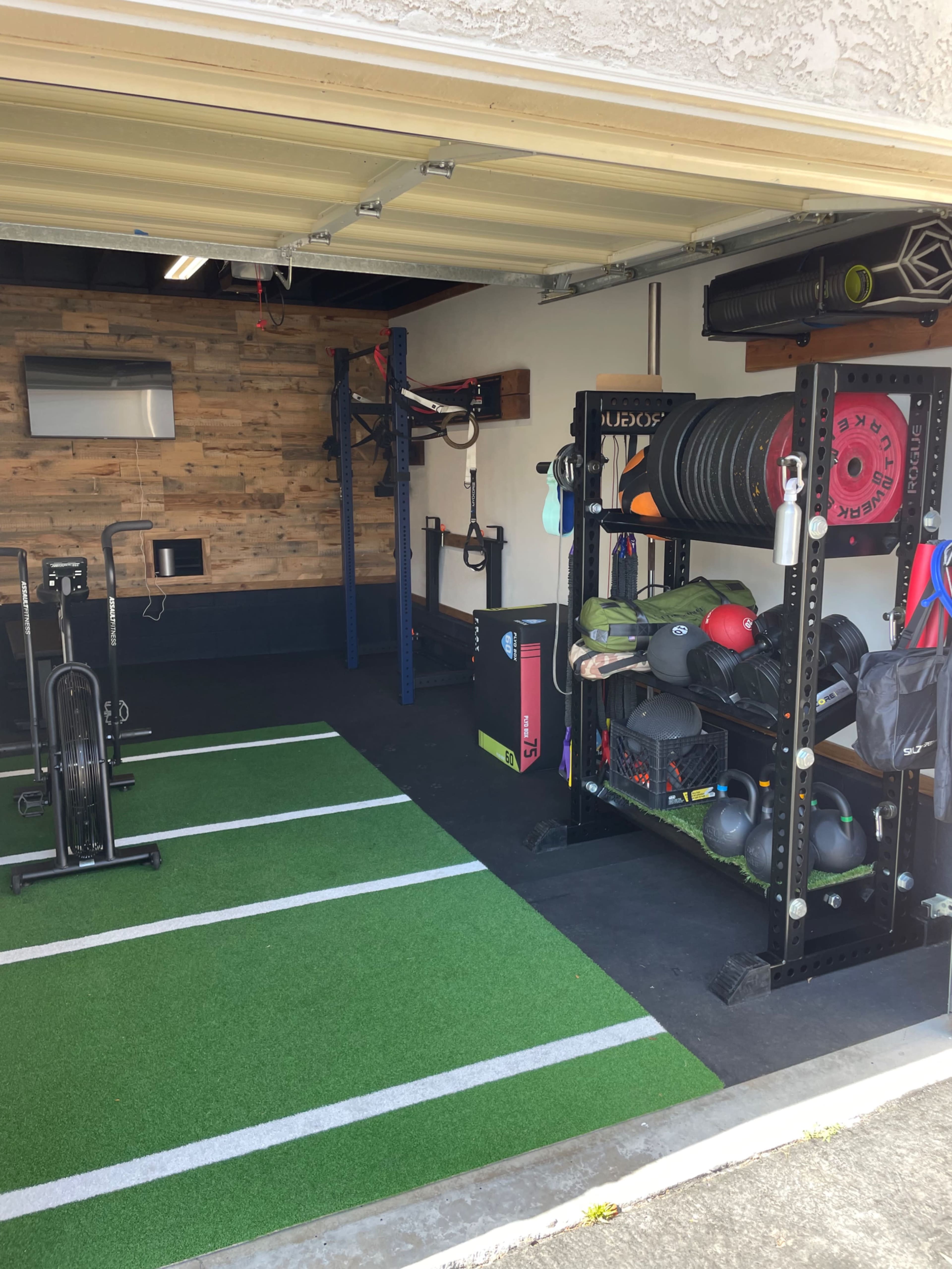 A home gym setup in a garage featuring workout equipment, including a rack of weights, exercise mats, and a stationary bike.
