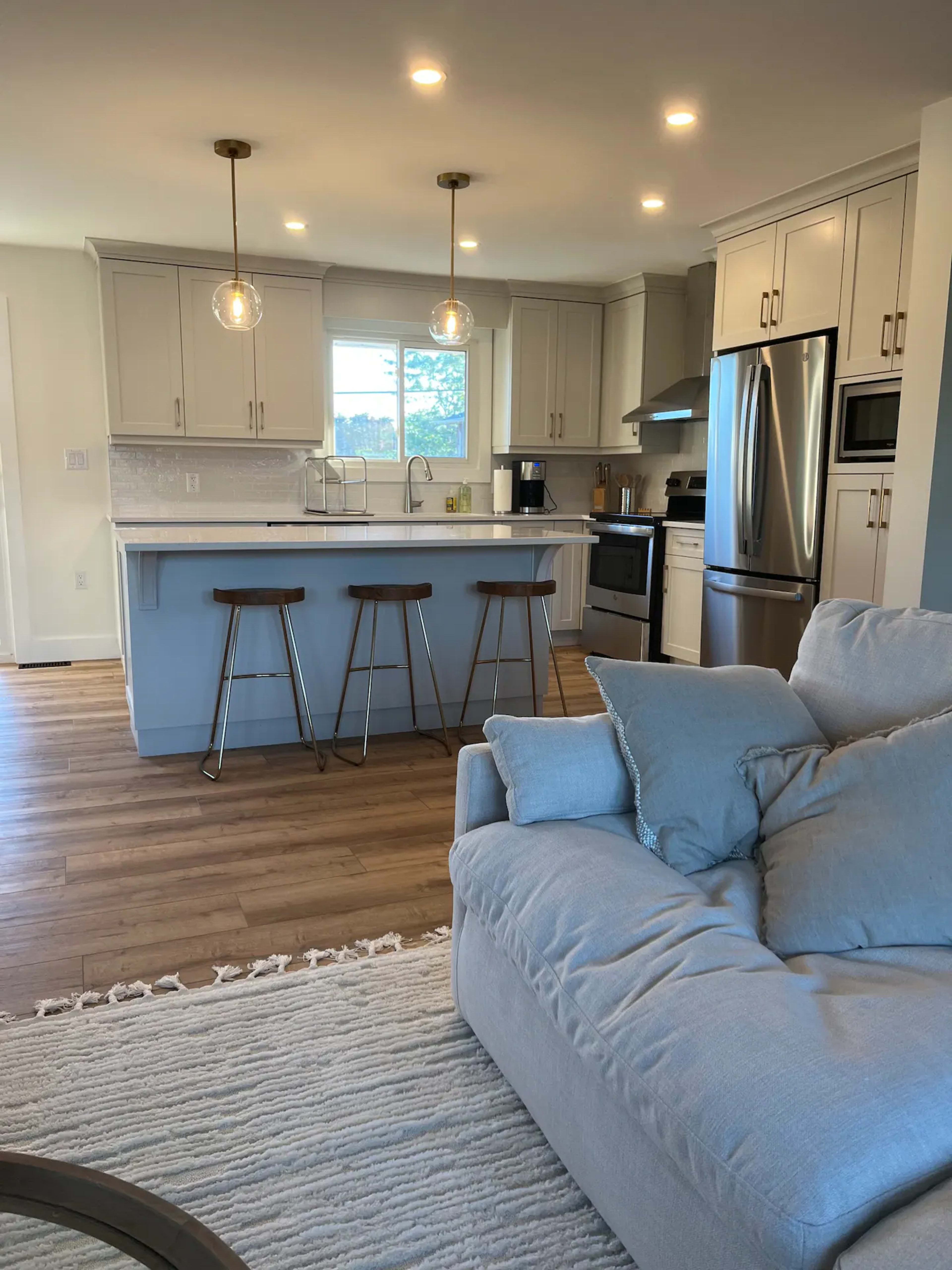 A modern kitchen with light cabinetry, stainless steel appliances, and a small dining area with three bar stools adjacent to the counter.