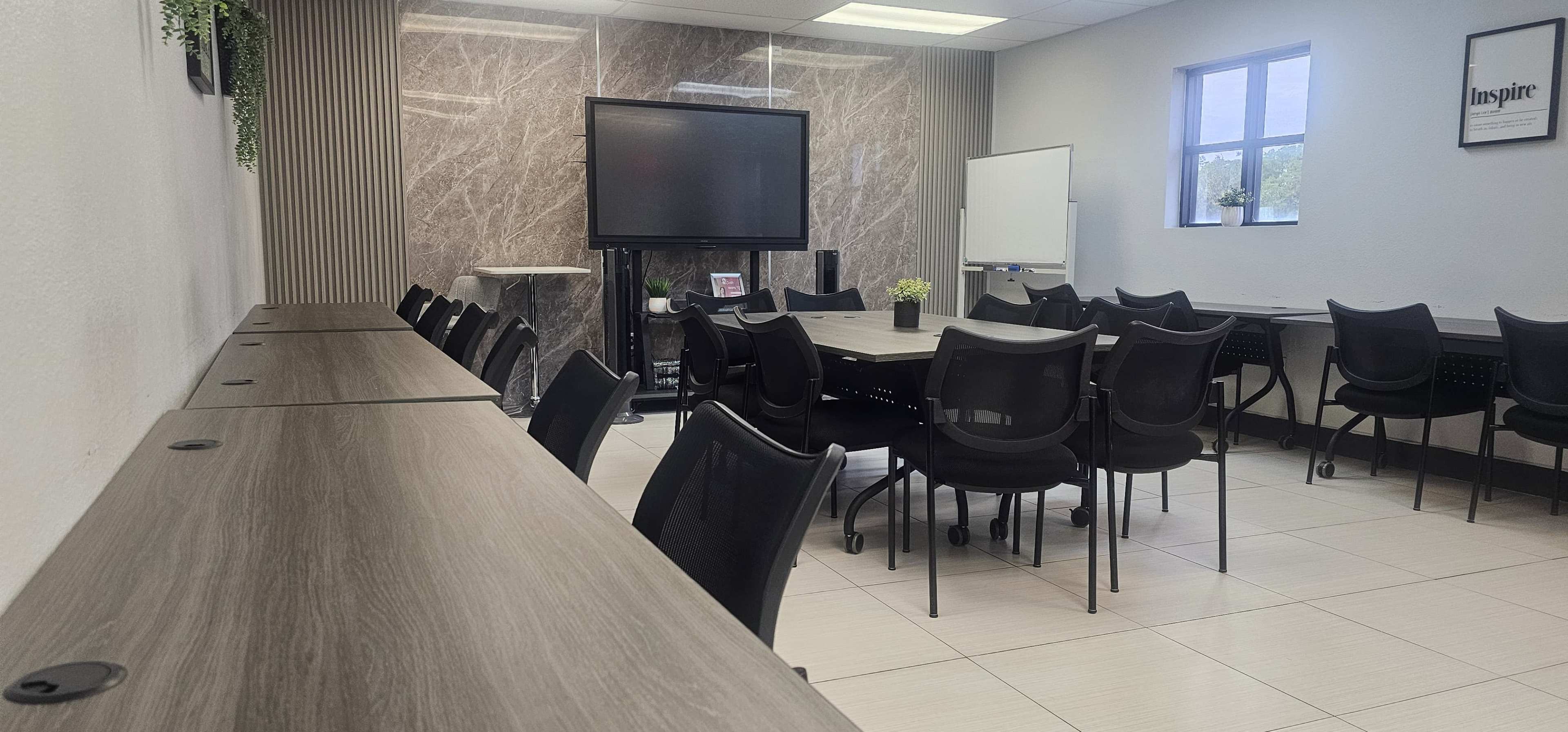 A modern conference room features a long table surrounded by black chairs, a large screen facing the seating area, and a whiteboard on one wall.