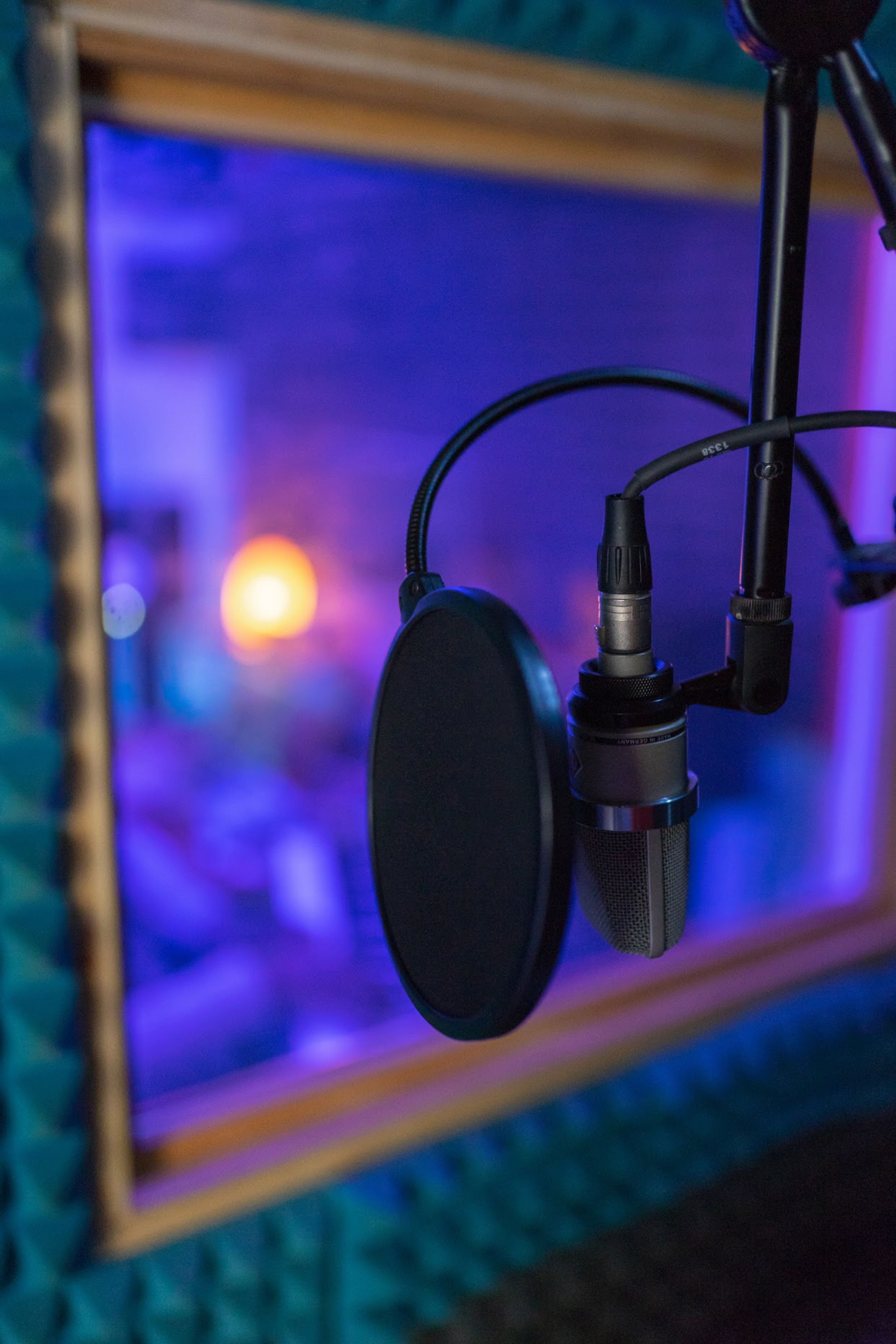 A microphone with a pop filter is hanging in front of a soundproofed recording booth.