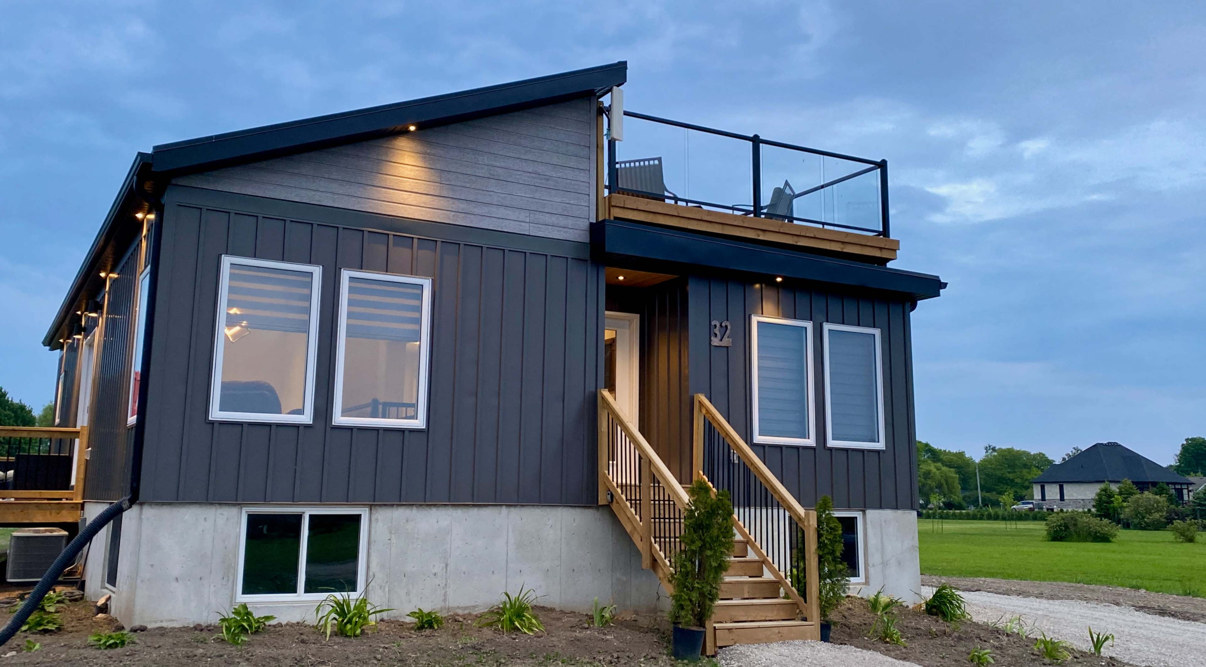 A modern two-story house with a wooden deck and railing, situated on a grassy lot.