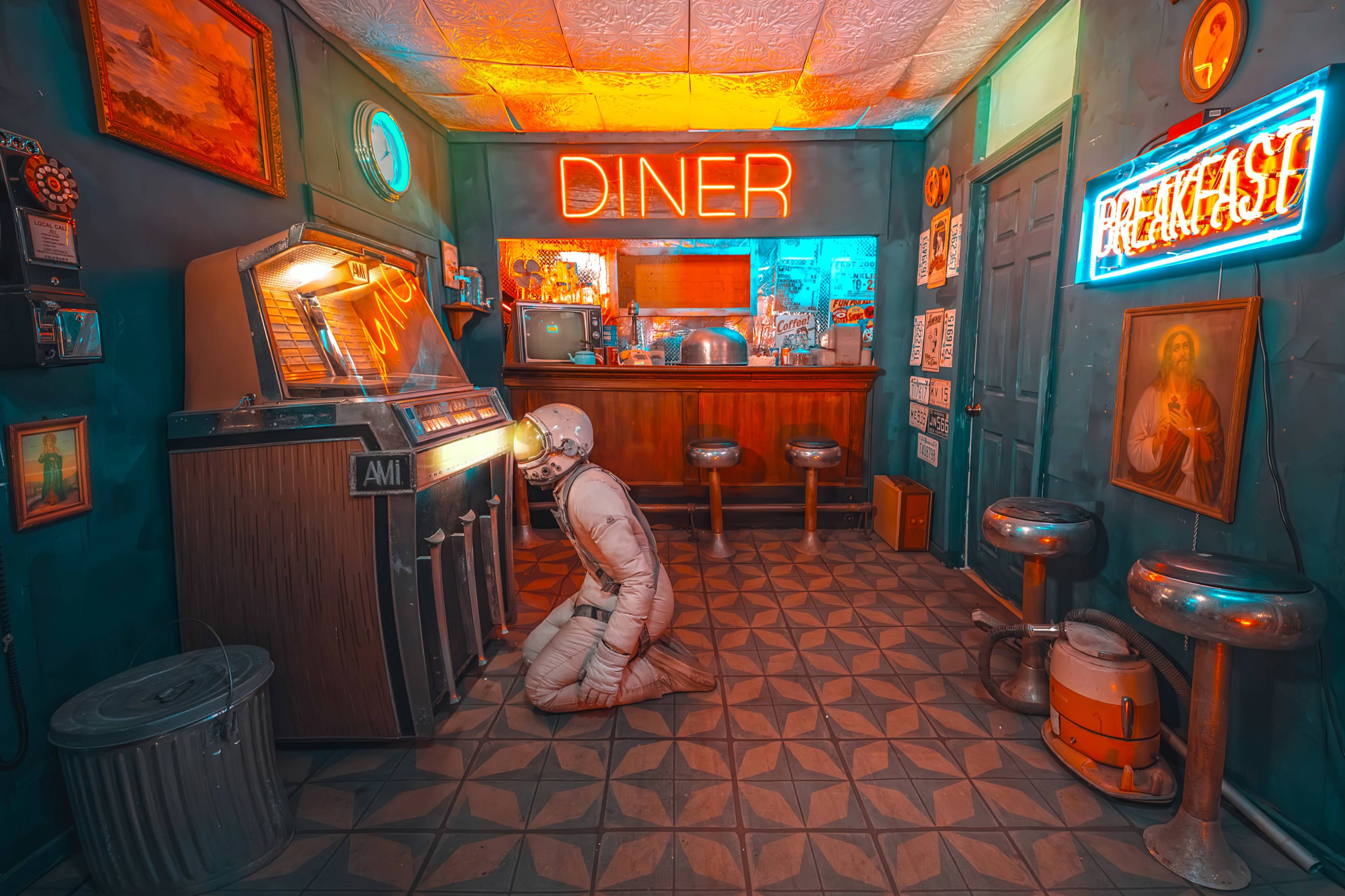 An astronaut kneels in a retro diner, operating a vintage jukebox under neon signs that read "DINER" and "BREAKFAST."