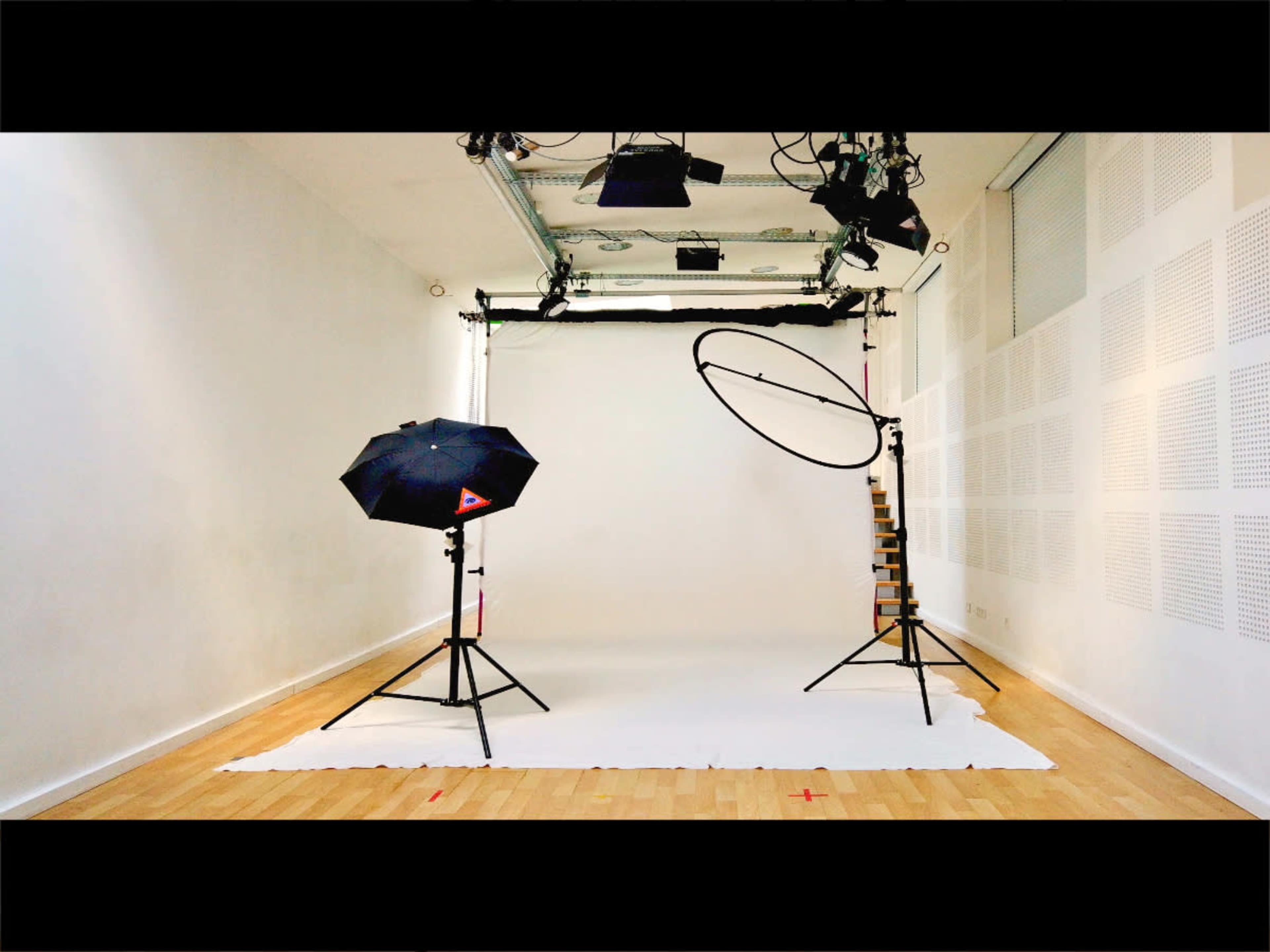 A photography studio with lighting equipment and a blank backdrop set up on a wooden floor.