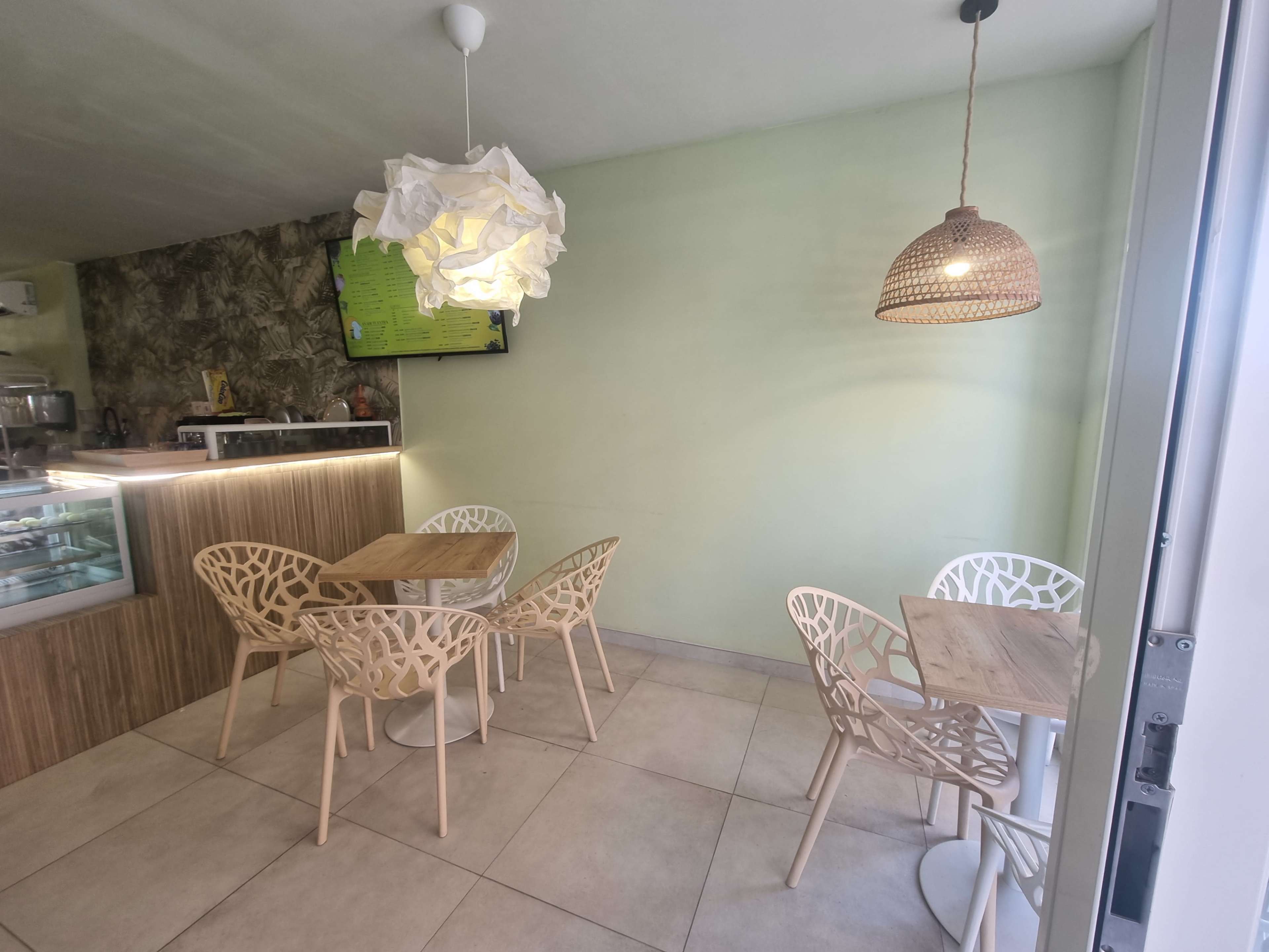 A small café interior features wooden tables and decorative chairs, with ambient lighting and a television mounted on the wall.