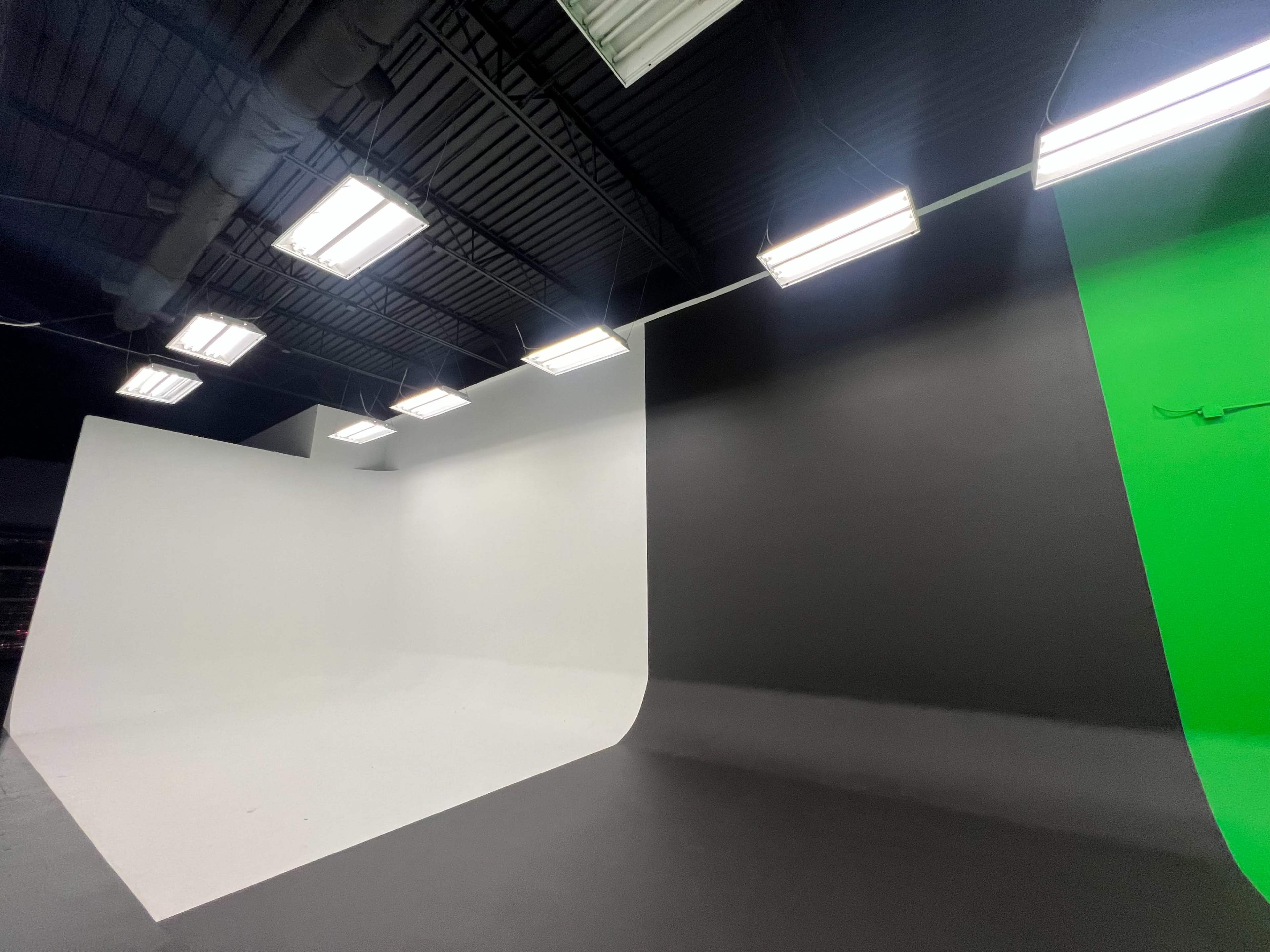 A studio space with three colored backdrops: white, black, and green, each forming a seamless curve on the floor.