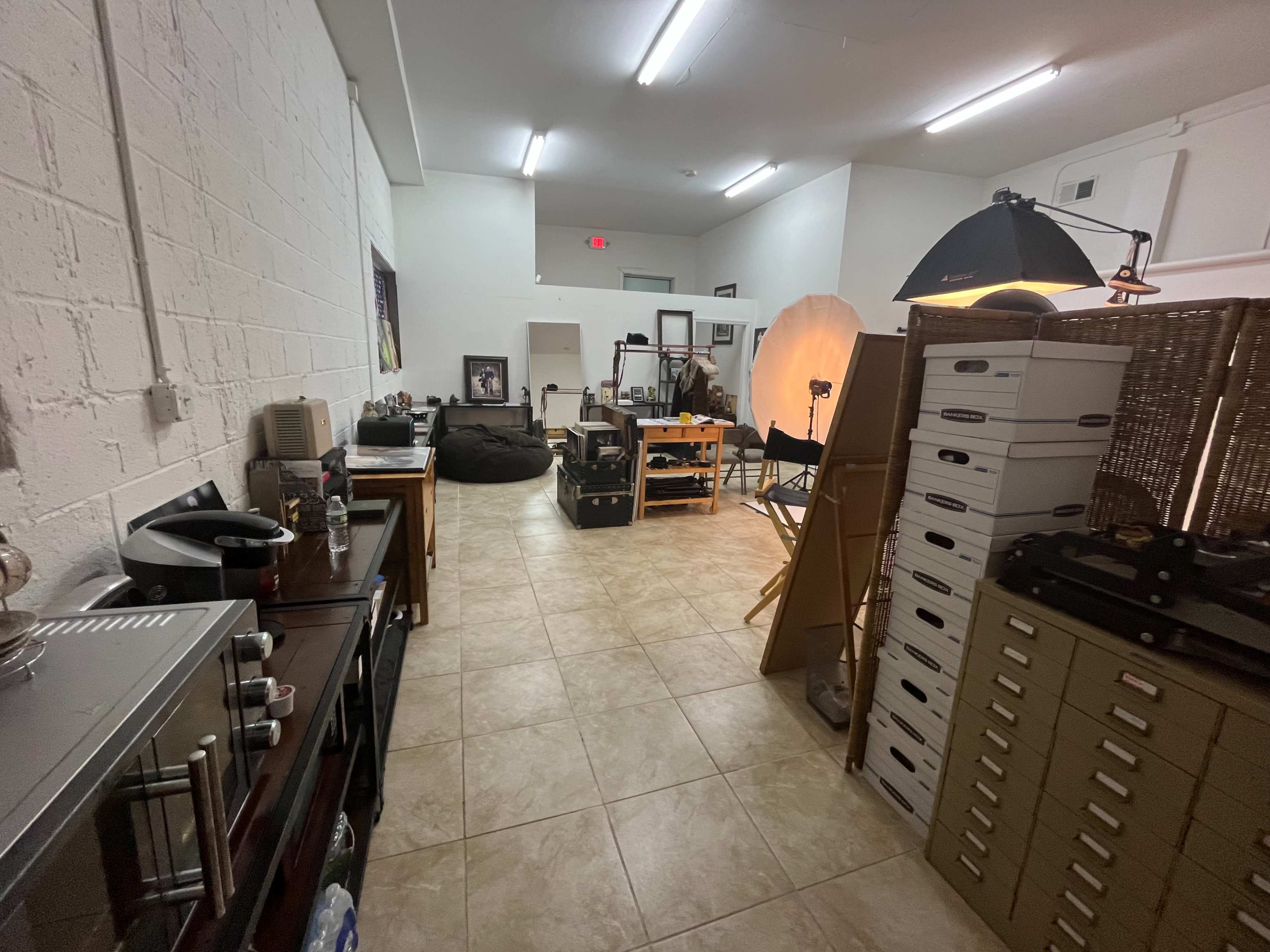 A spacious room with tiled floors, featuring various furniture items, photography equipment, and storage boxes.