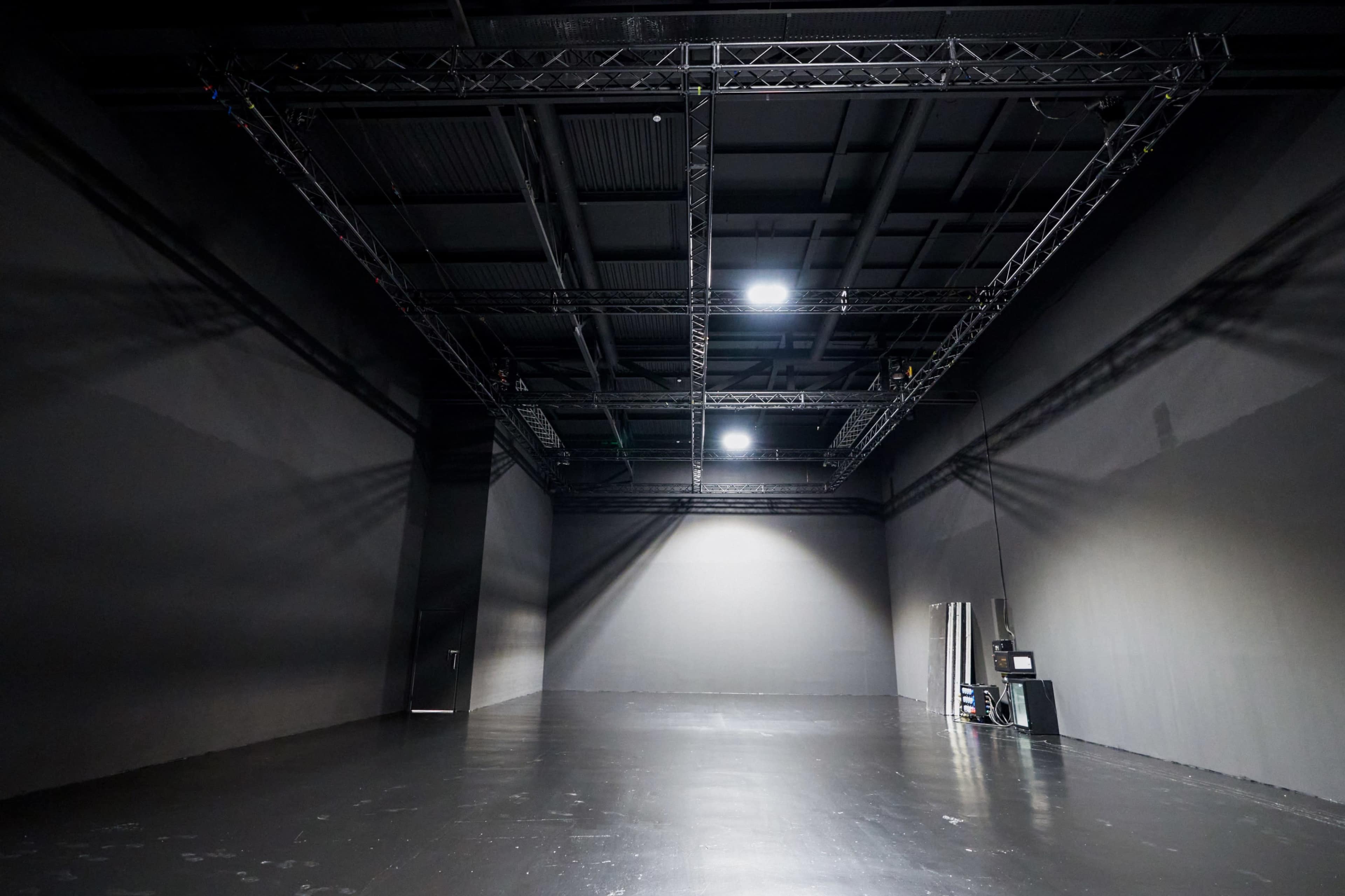 The image shows a large, empty studio space with dark walls, a polished floor, and industrial lighting overhead.