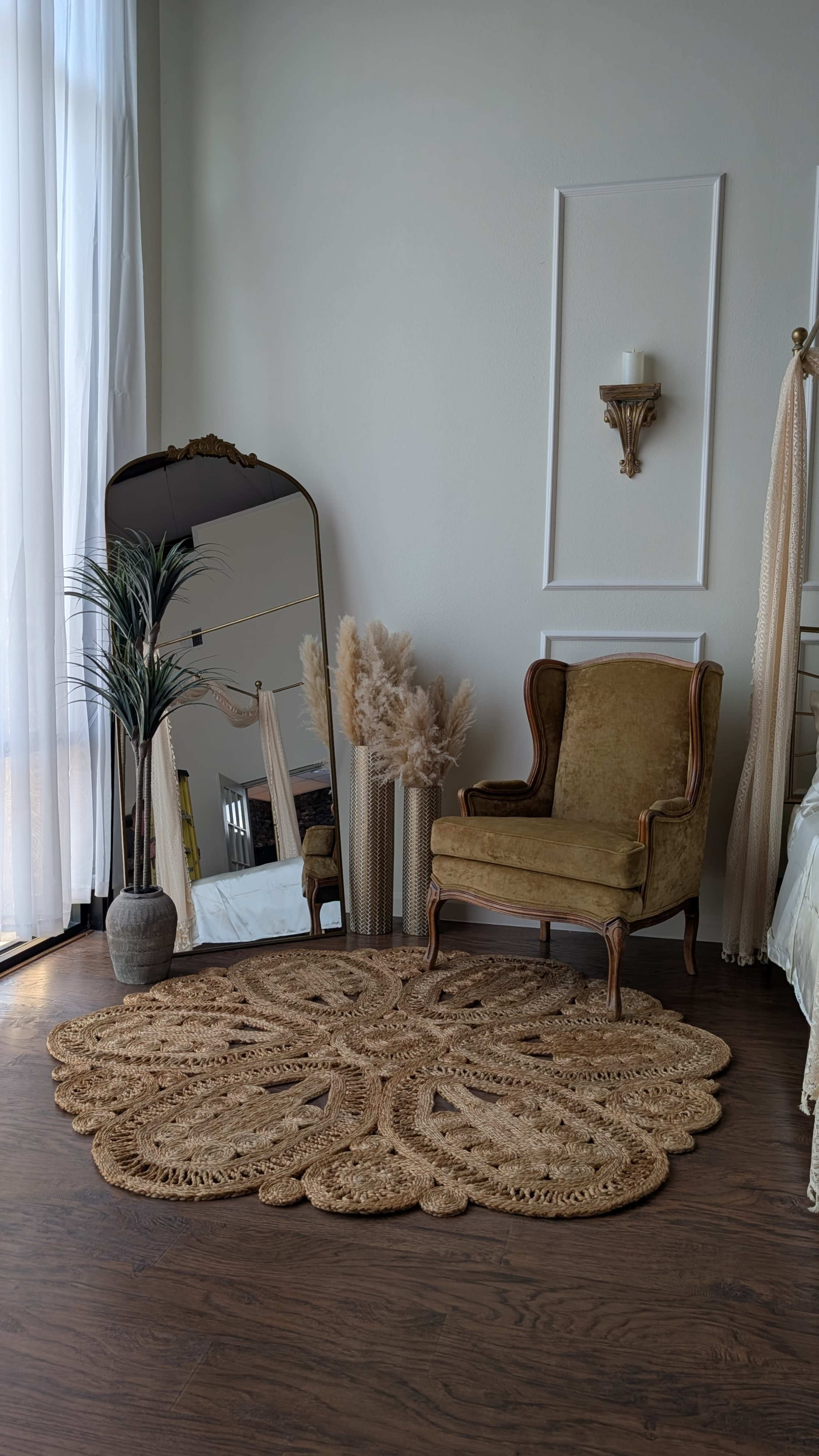 A vintage armchair sits beside a large mirror and decorative plants in a softly lit corner of a room with a patterned rug.