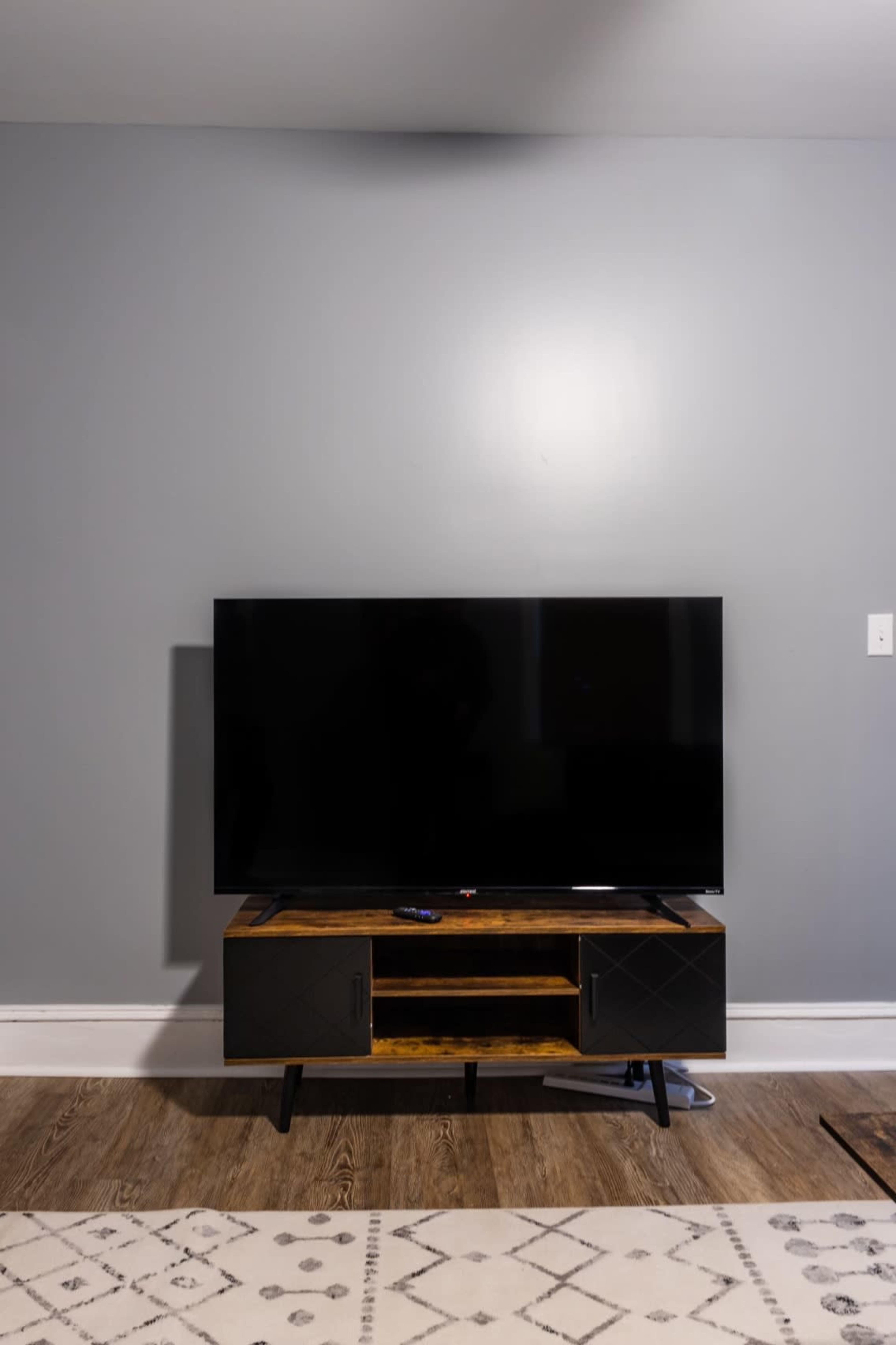A black television is placed on a wooden stand against a gray wall in a room with a light-colored rug.
