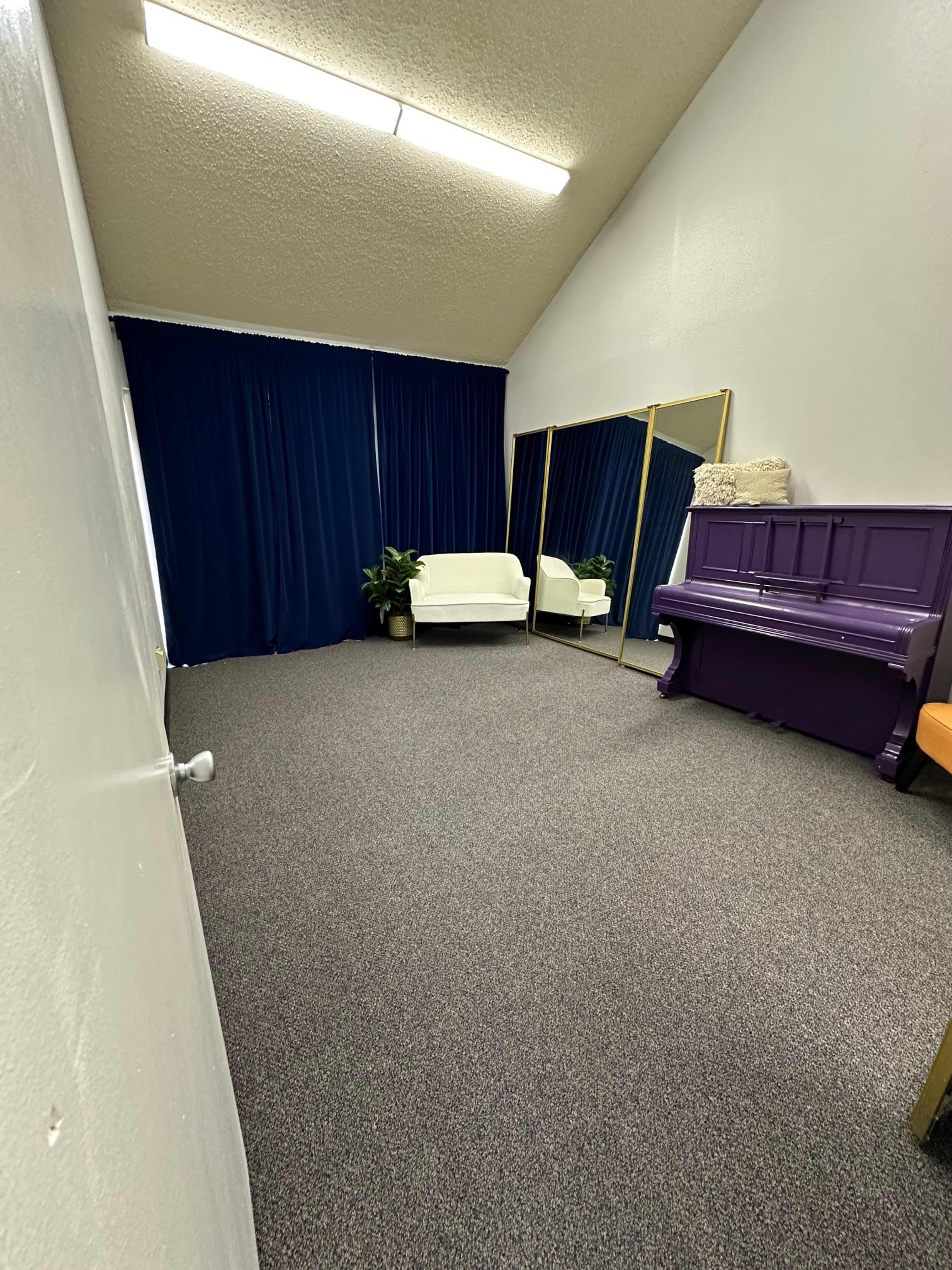 The image shows a spacious room with a white sofa, a large mirror, a purple piano, and dark blue curtains.