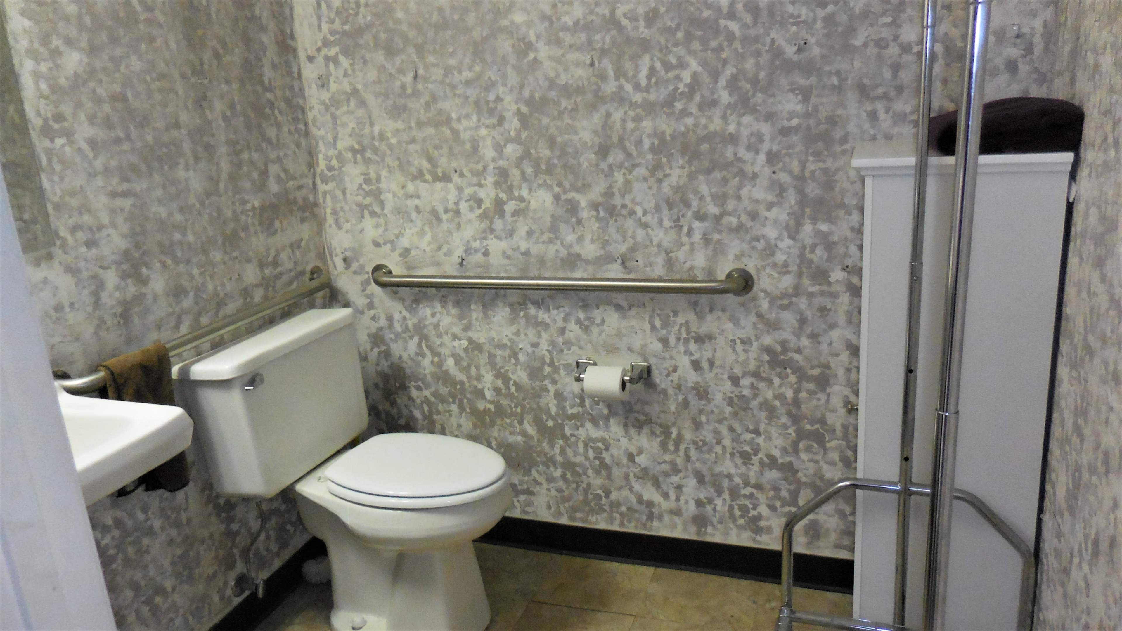 A small bathroom featuring a toilet, a sink, a towel rack, a shower stall, and a storage cabinet against a textured wall.