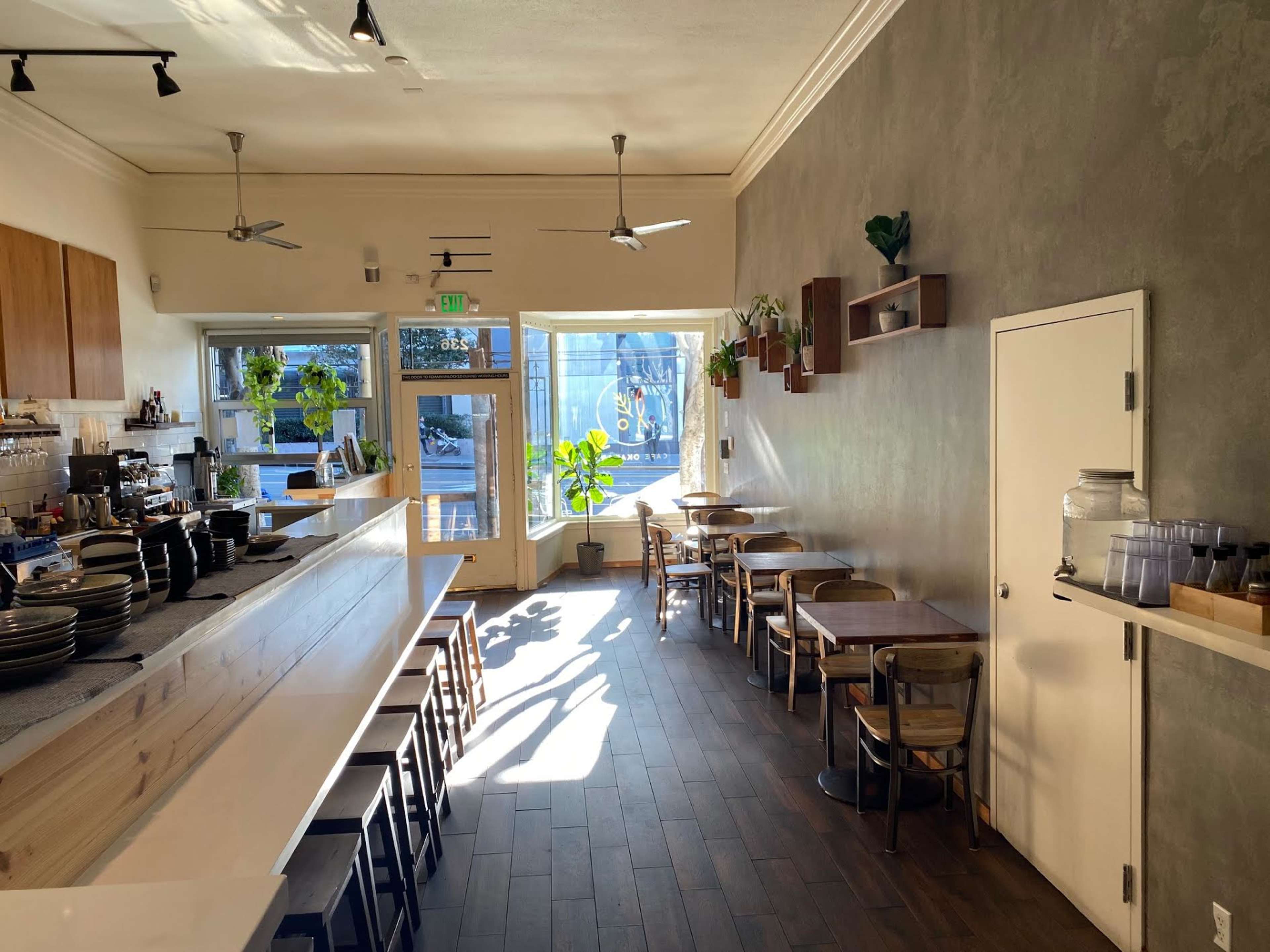 A modern café with a long wooden counter, several tables, and large windows letting in natural light.