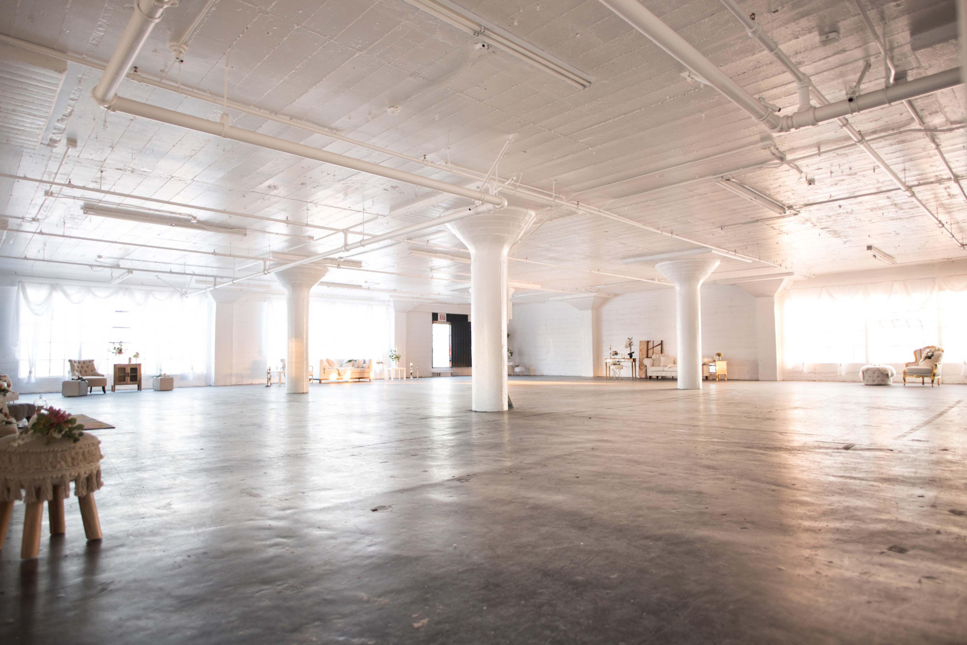 A spacious, empty industrial-style room with polished concrete floors and large windows letting in natural light.