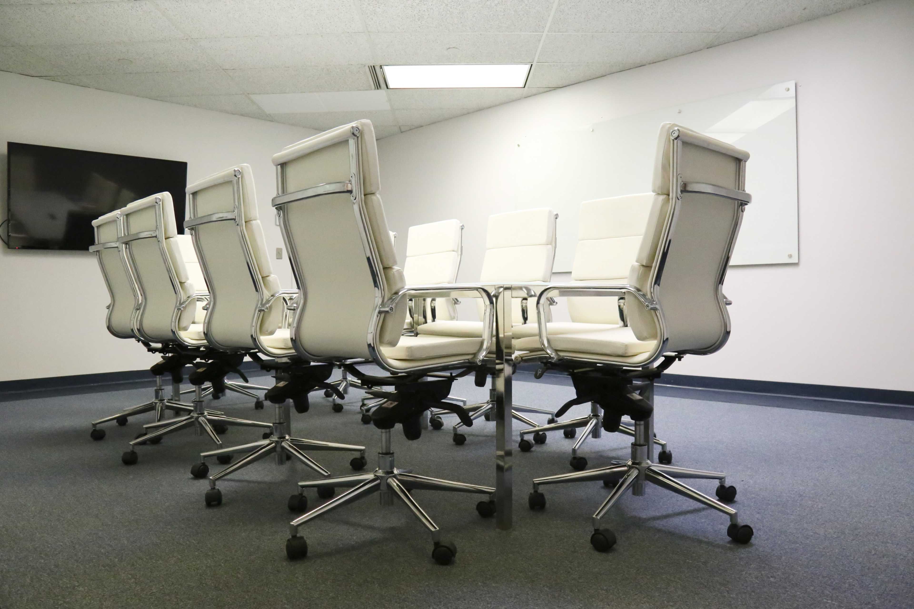 A row of white leather office chairs on rolling bases is arranged around a conference table in a meeting room.