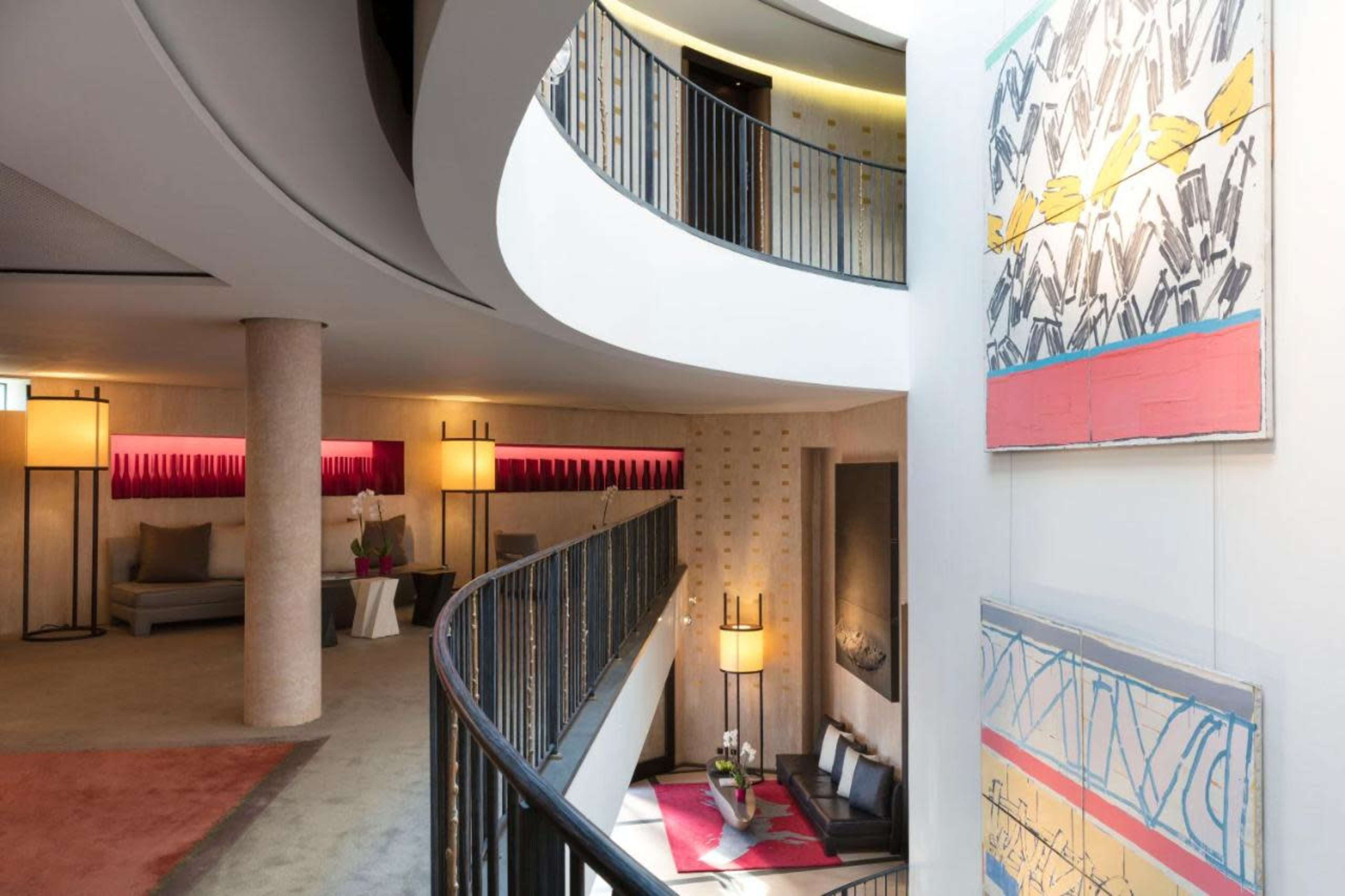 A modern interior space with a curved staircase, artistic wall decorations, and a seating area illuminated by lamps.