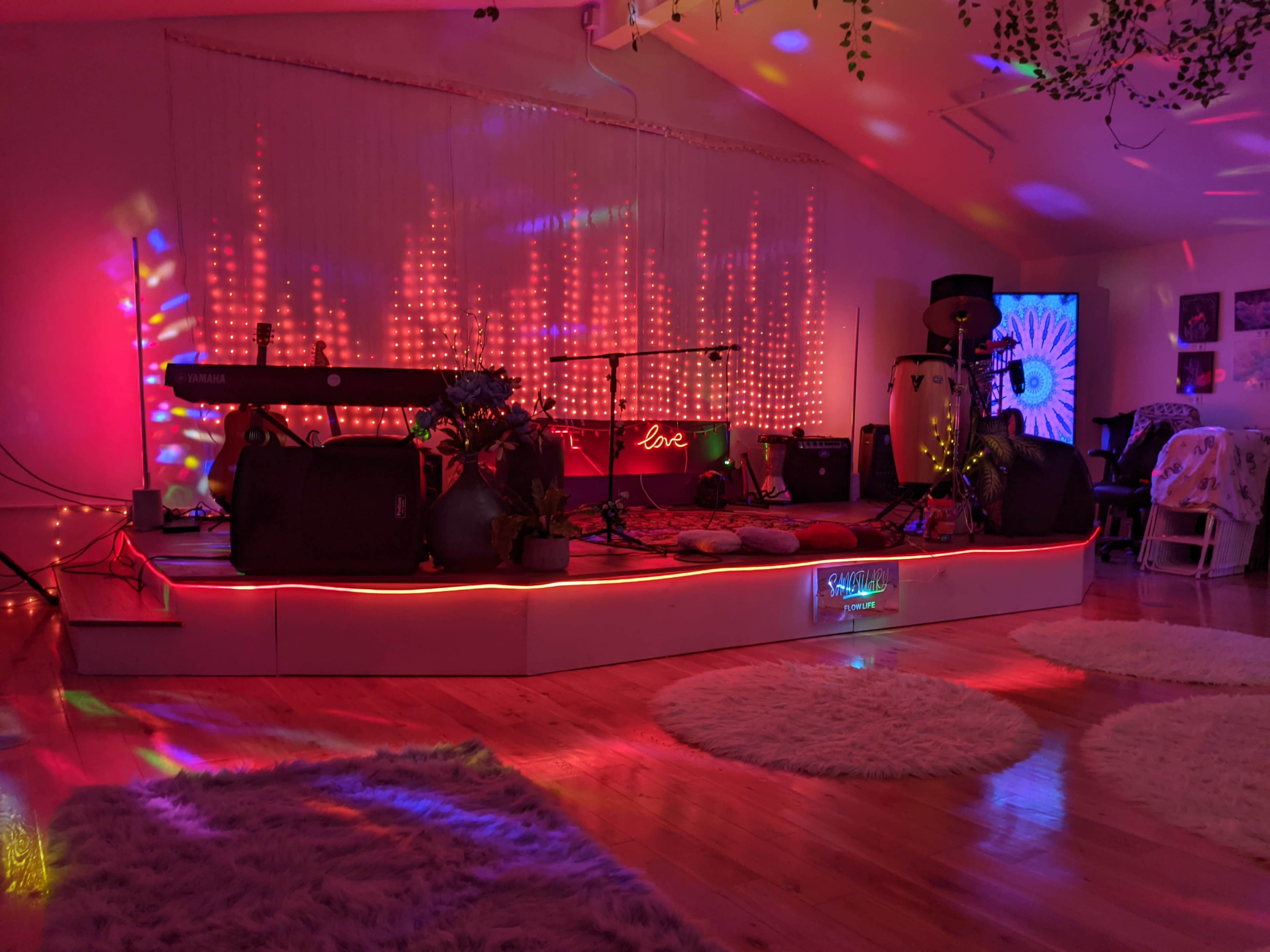 The scene features a stage adorned with colorful lights and musical instruments, including a keyboard and conga drums, set in a warmly lit room.
