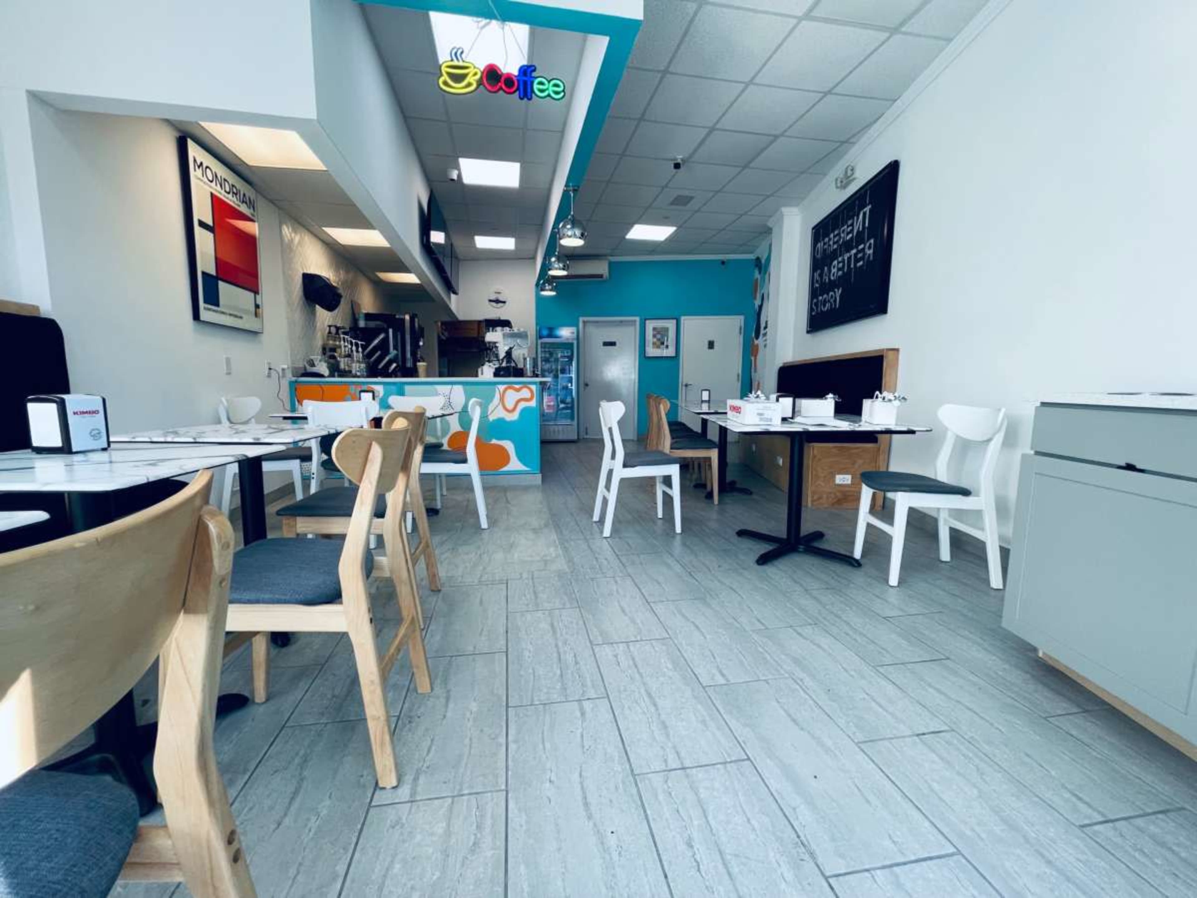A bright café interior features several tables and chairs, with a colorful service counter in the background.