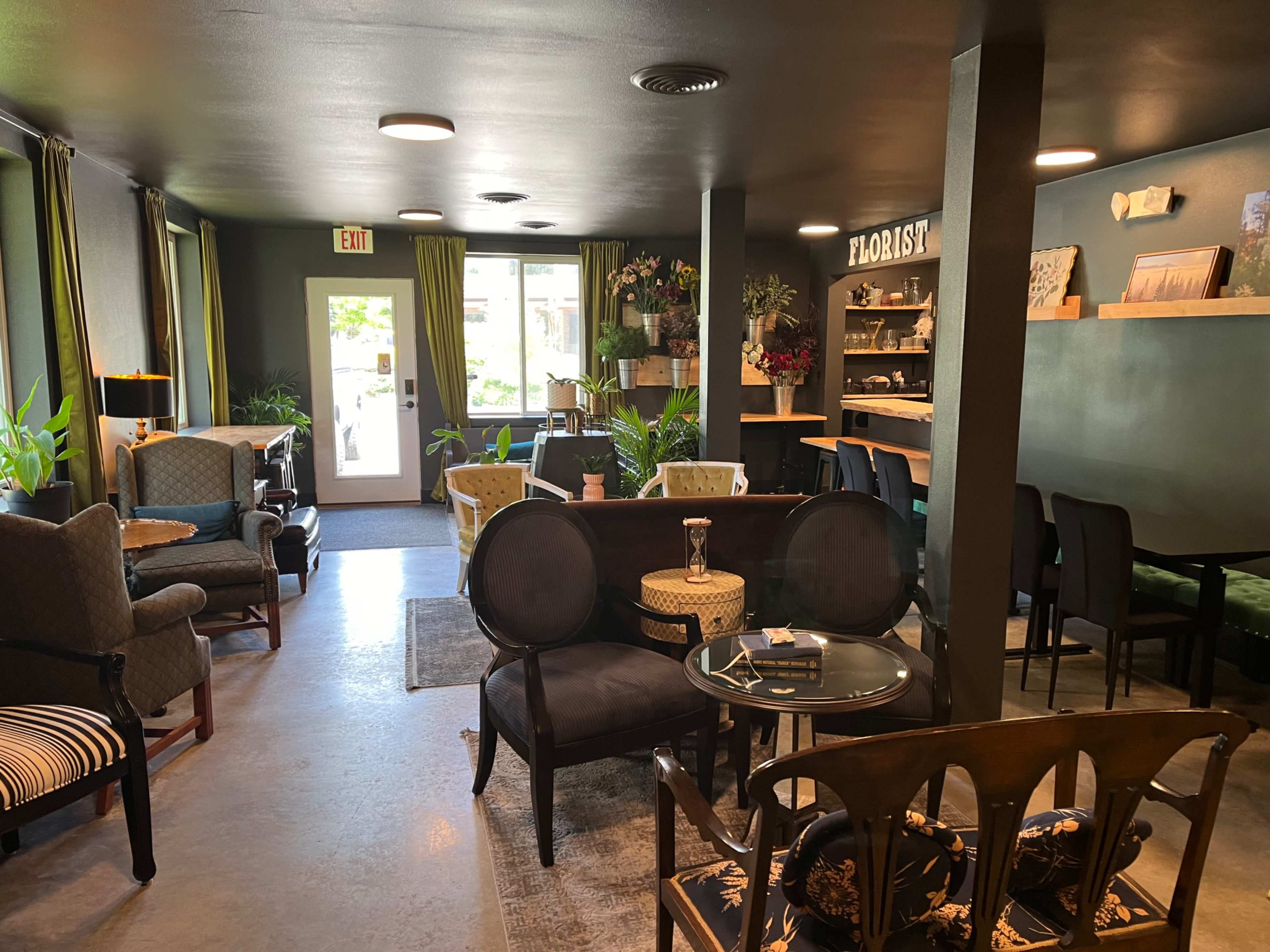 A cozy floral shop interior with various seating arrangements and decorative plants, complemented by a small counter area.