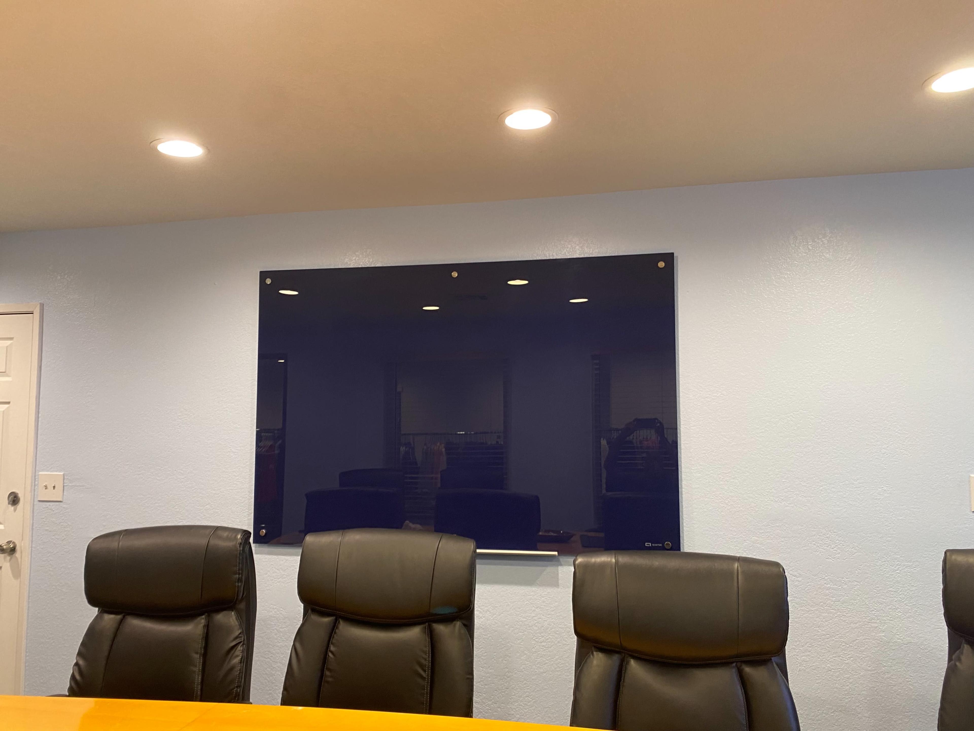 A conference room features a long wooden table and black leather chairs, with a large dark blue presentation board mounted on the wall.