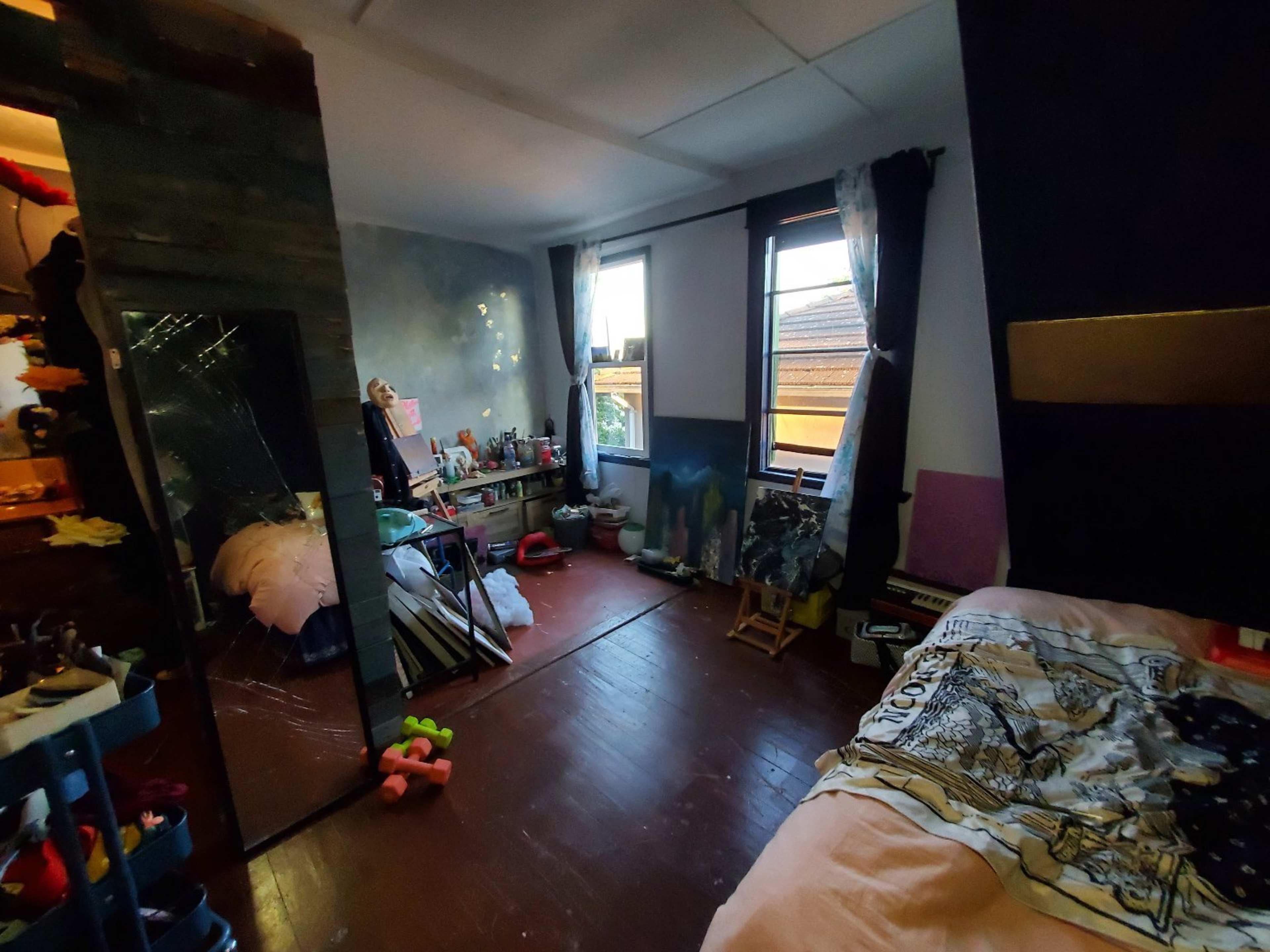 A cluttered bedroom featuring a bed, a mirror, and various personal items scattered around.