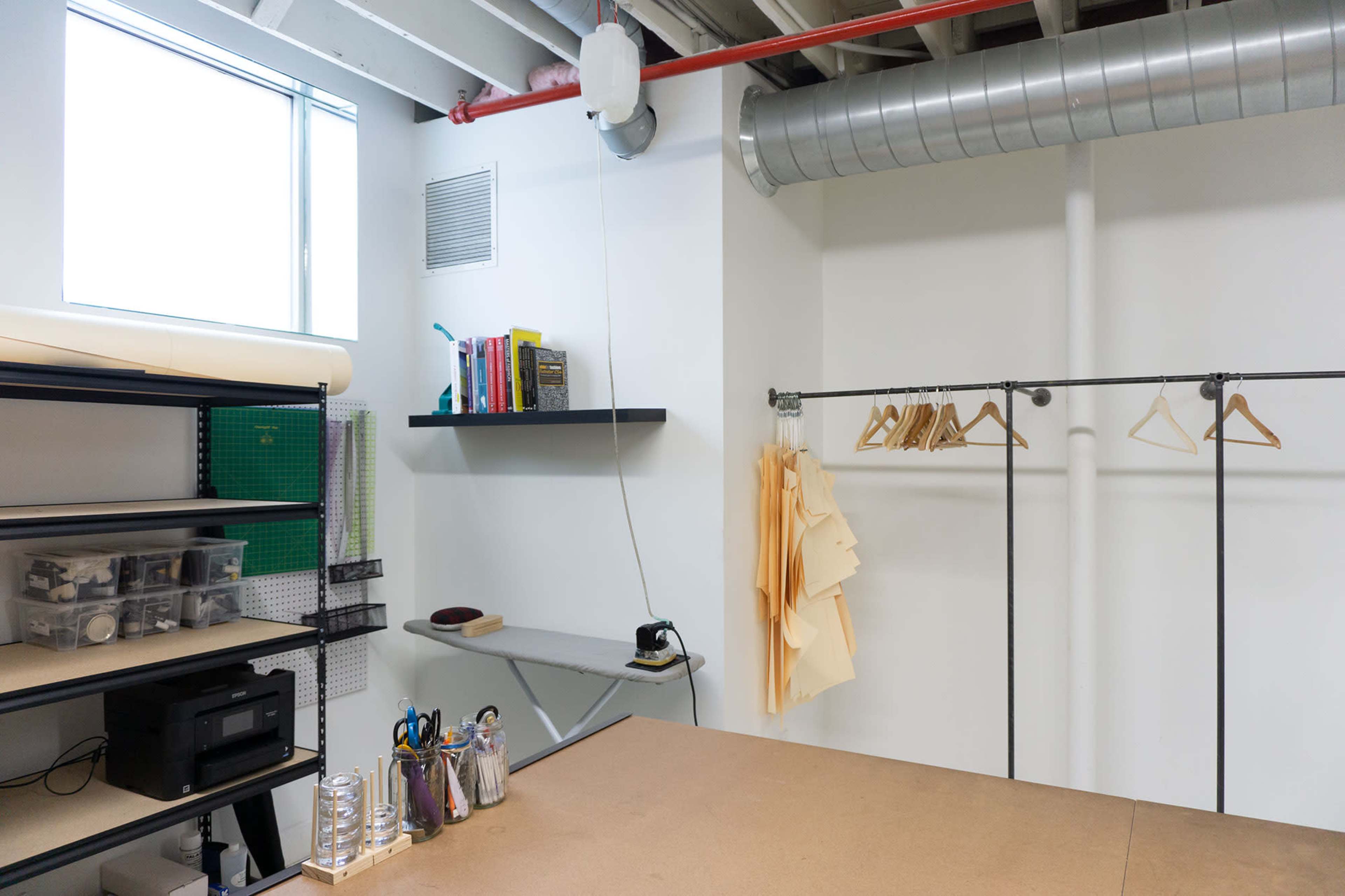 A minimalist workspace featuring shelving units, a hanging rack with wooden hangers, and a well-lit table area.