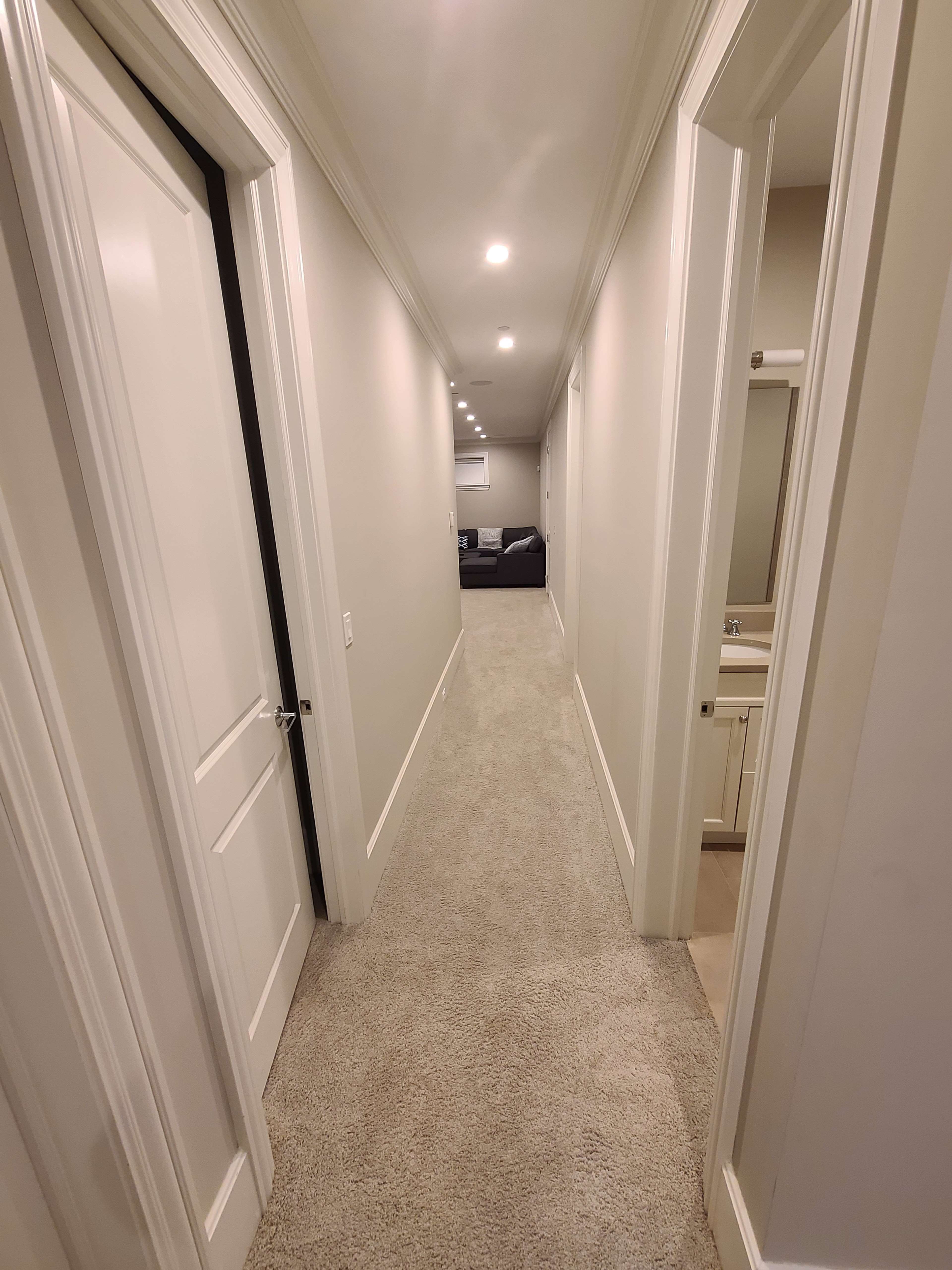 A long hallway with beige carpet and white doors leads to a room at the end, partially visible.