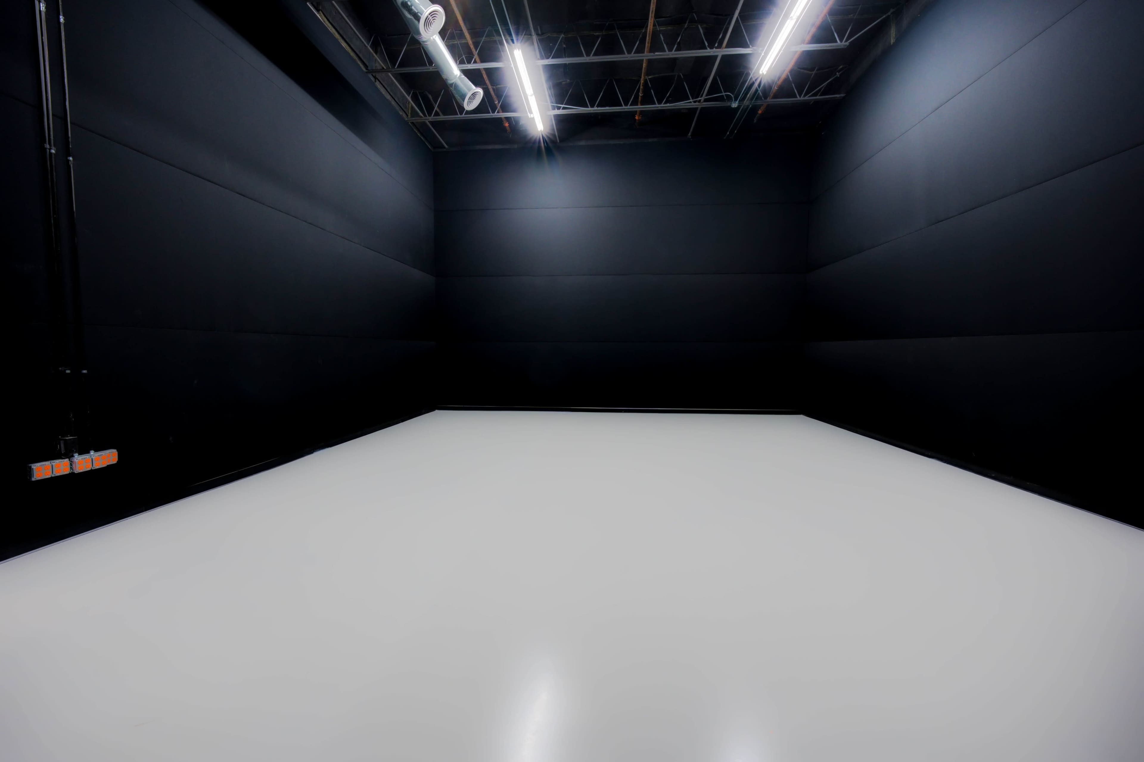 A large, empty room with black walls and a white floor, illuminated by overhead lights.