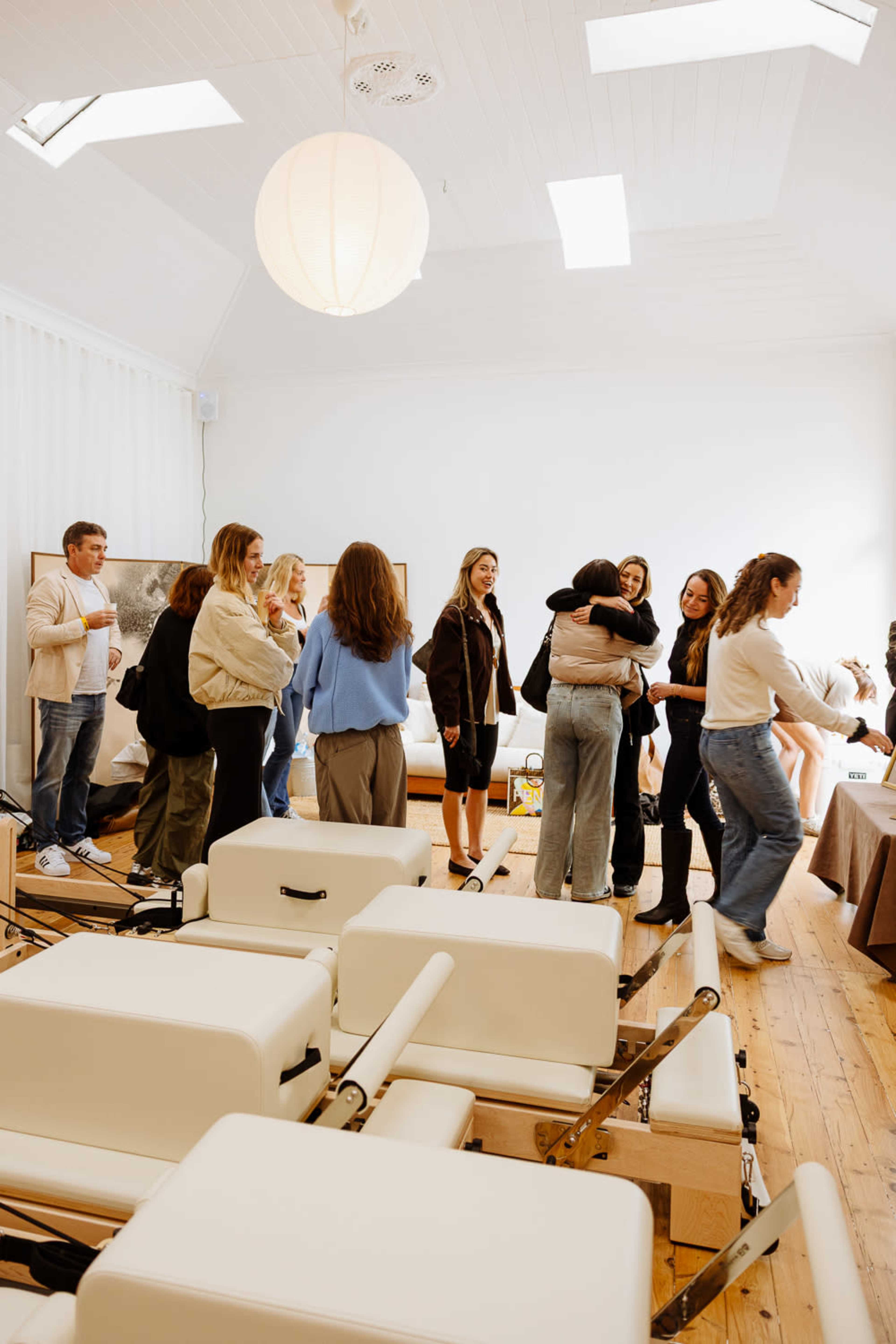 A group of people stands in a bright, airy studio with fitness equipment, engaging in conversation and friendly interactions.