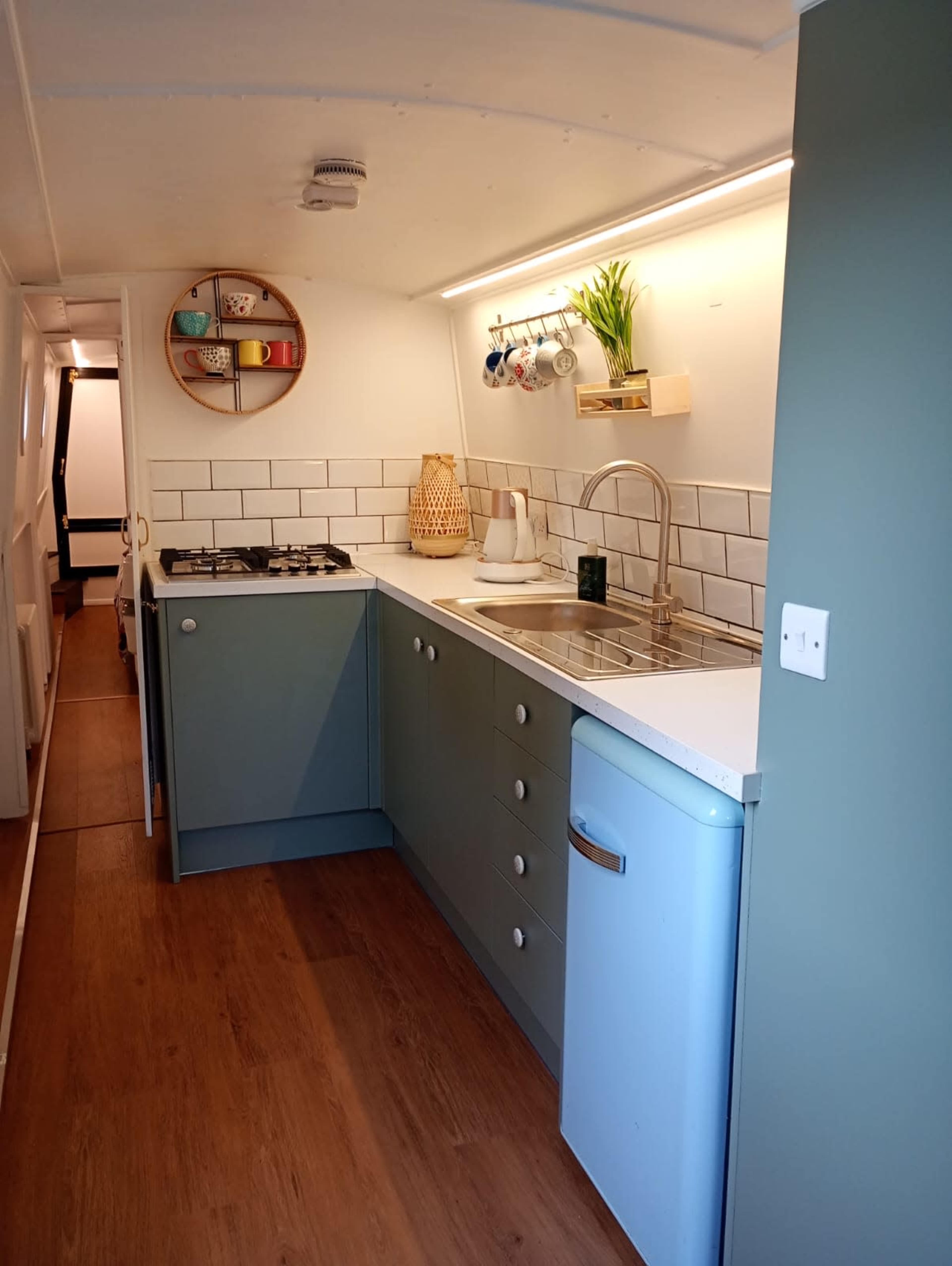 The image shows a modern kitchen in a small space featuring a gas stove, a sink, light wood accents, and pastel-colored cabinetry.