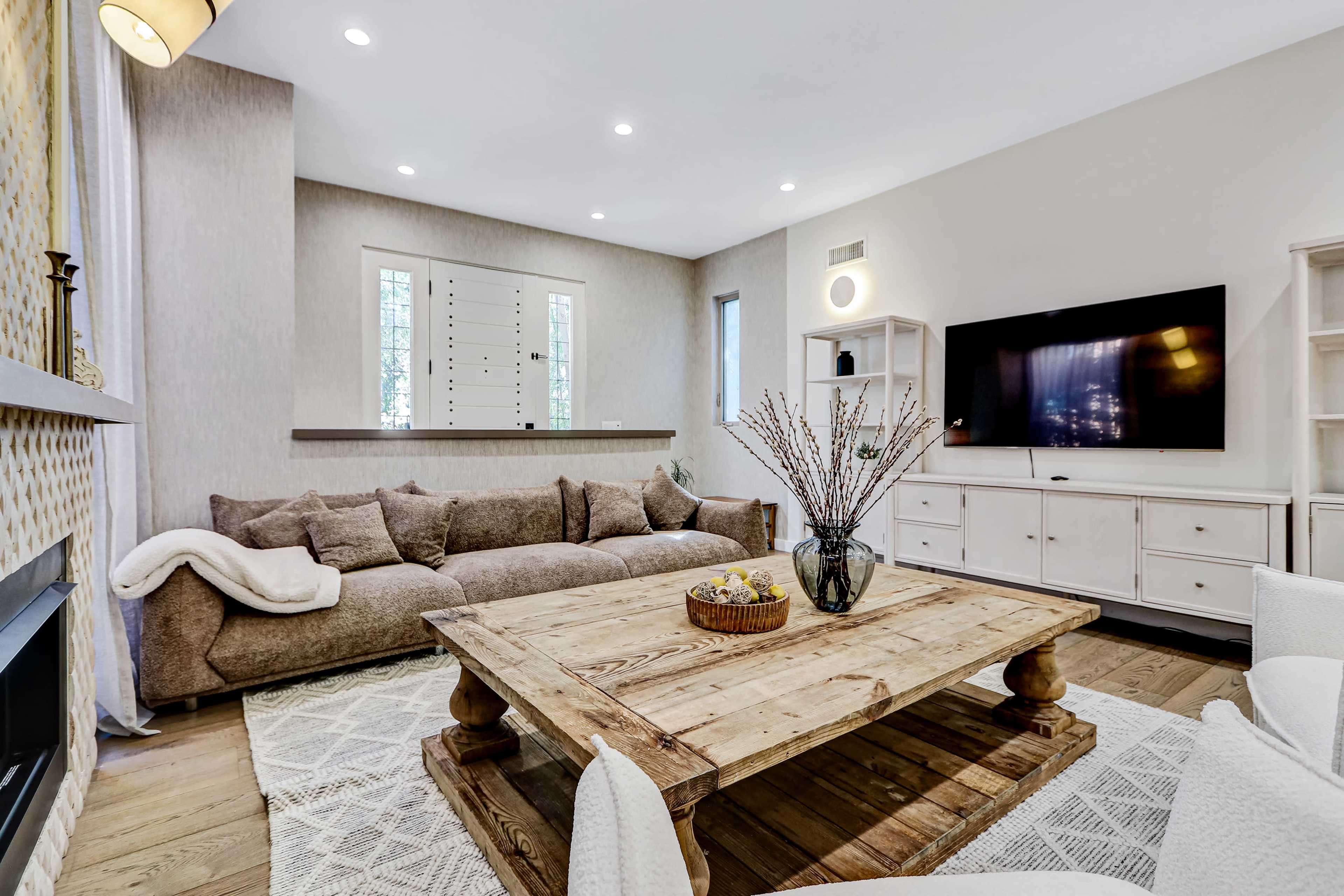 The image shows a modern living room with a large brown sofa, a wooden coffee table, and a wall-mounted television.