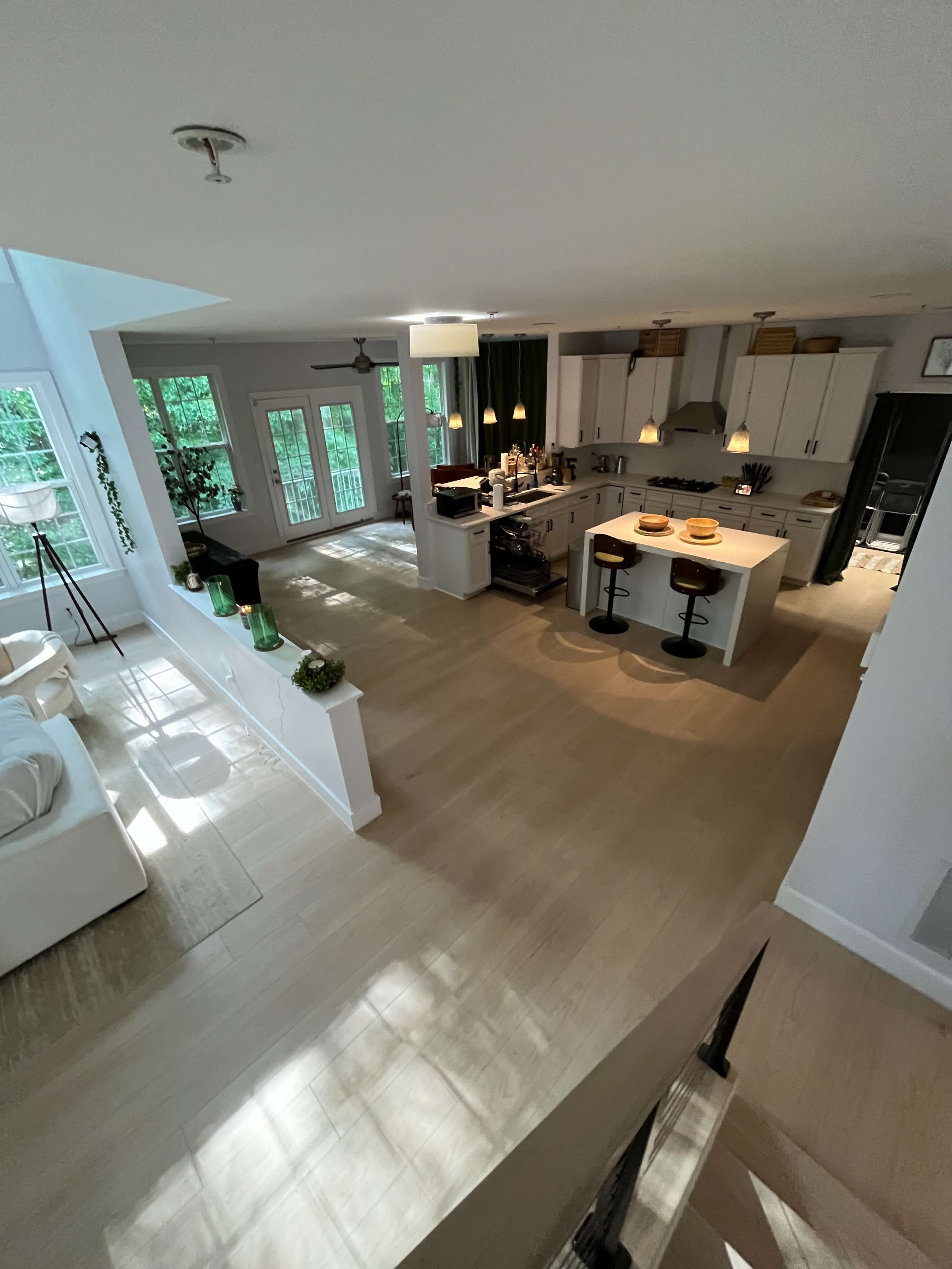 The image shows a spacious, modern kitchen adjacent to a dining area with a seating arrangement and large windows allowing natural light to flow in.