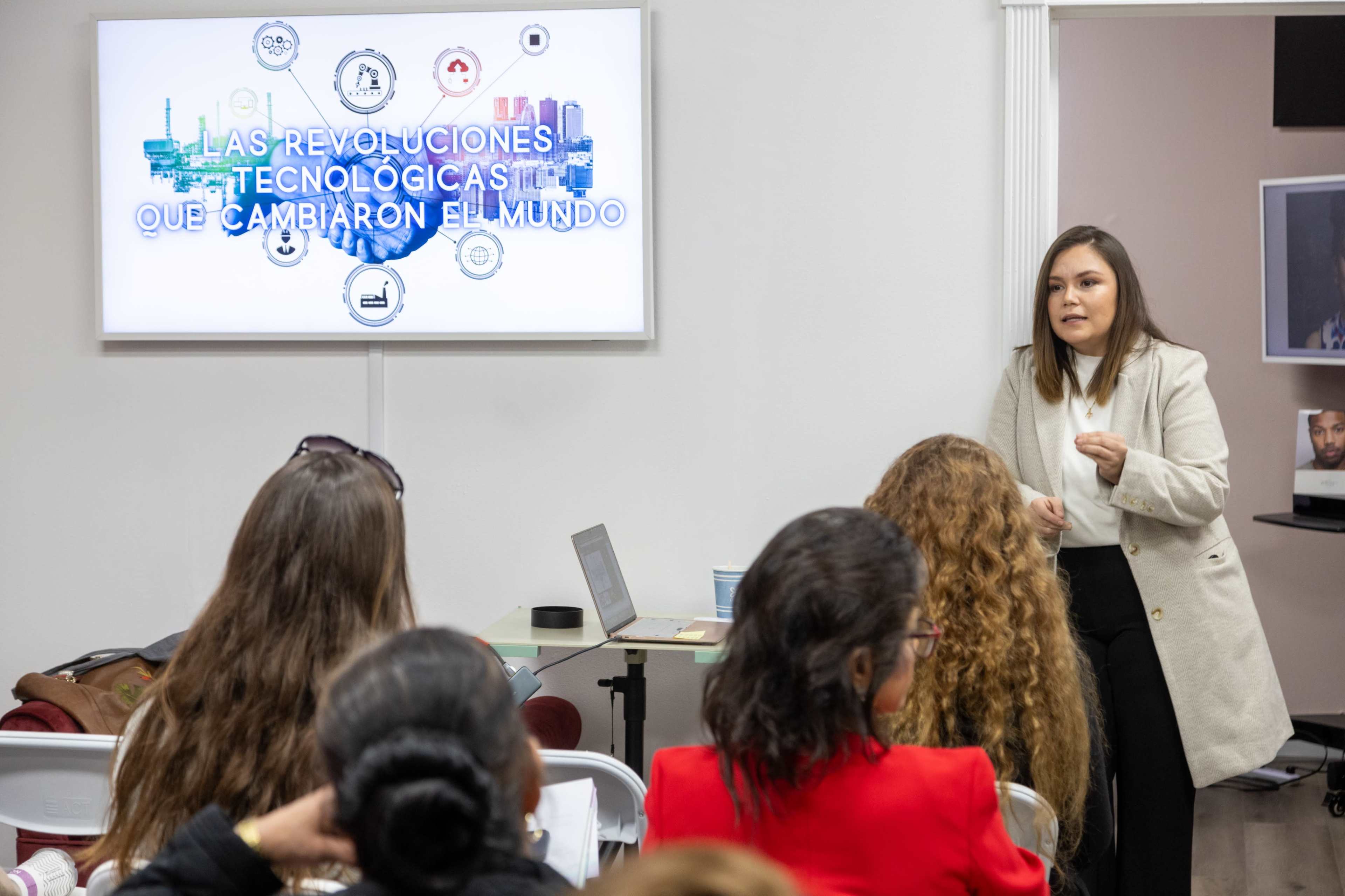 A speaker presents on technological revolutions in front of an audience, with a projection screen displaying the title of the presentation.
